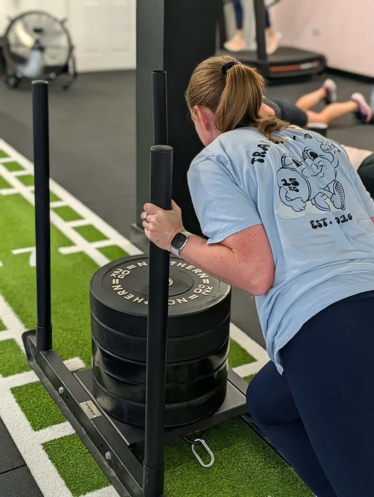 Woman pushing a weight sled in a gym.