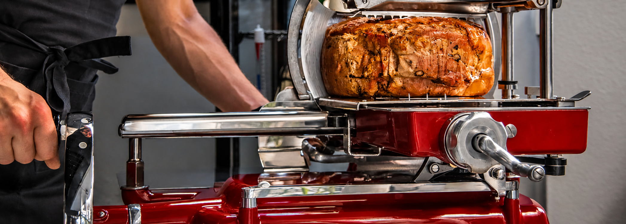 Un Jambon truffée tranché dans une machine à couper Berkel manuelle, un homme en noir coupe la viande.