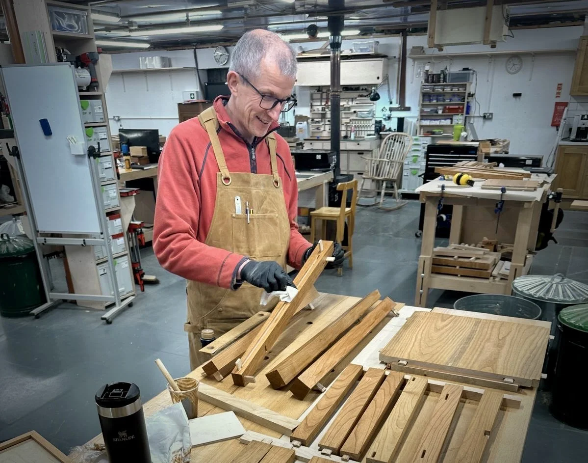 Woodworker wearing an apron assembles wooden furniture parts in a workshop.
