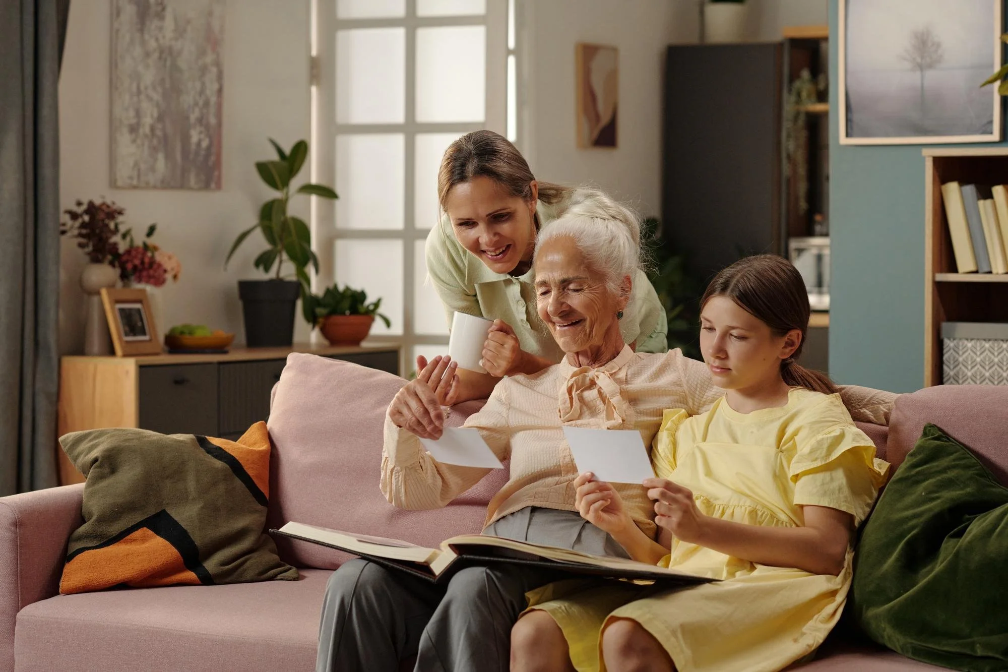 Senior woman looking through family photo albums with her daughter and granddaughter, reflecting the compassionate senior downsizing services of Sweet Transitions LLC.