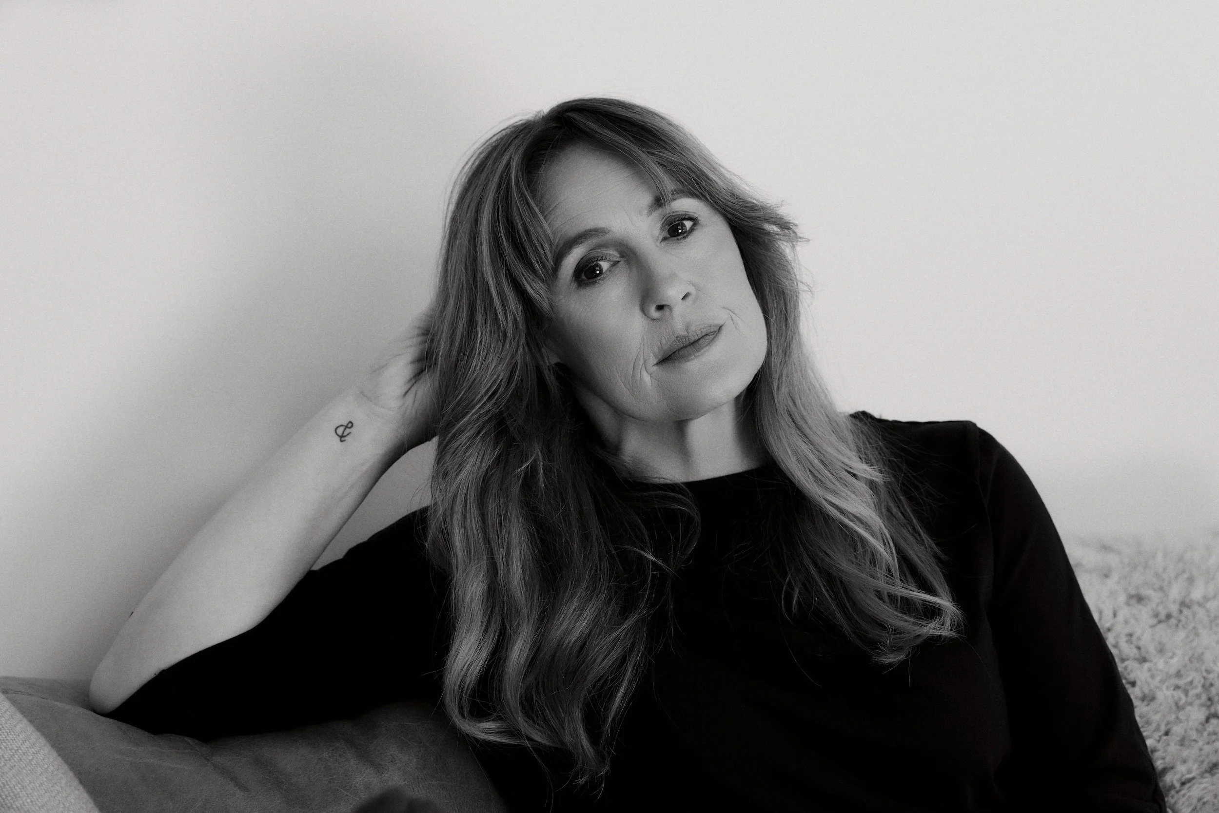Black-and-white portrait of a smiling woman with long hair sitting on a couch.