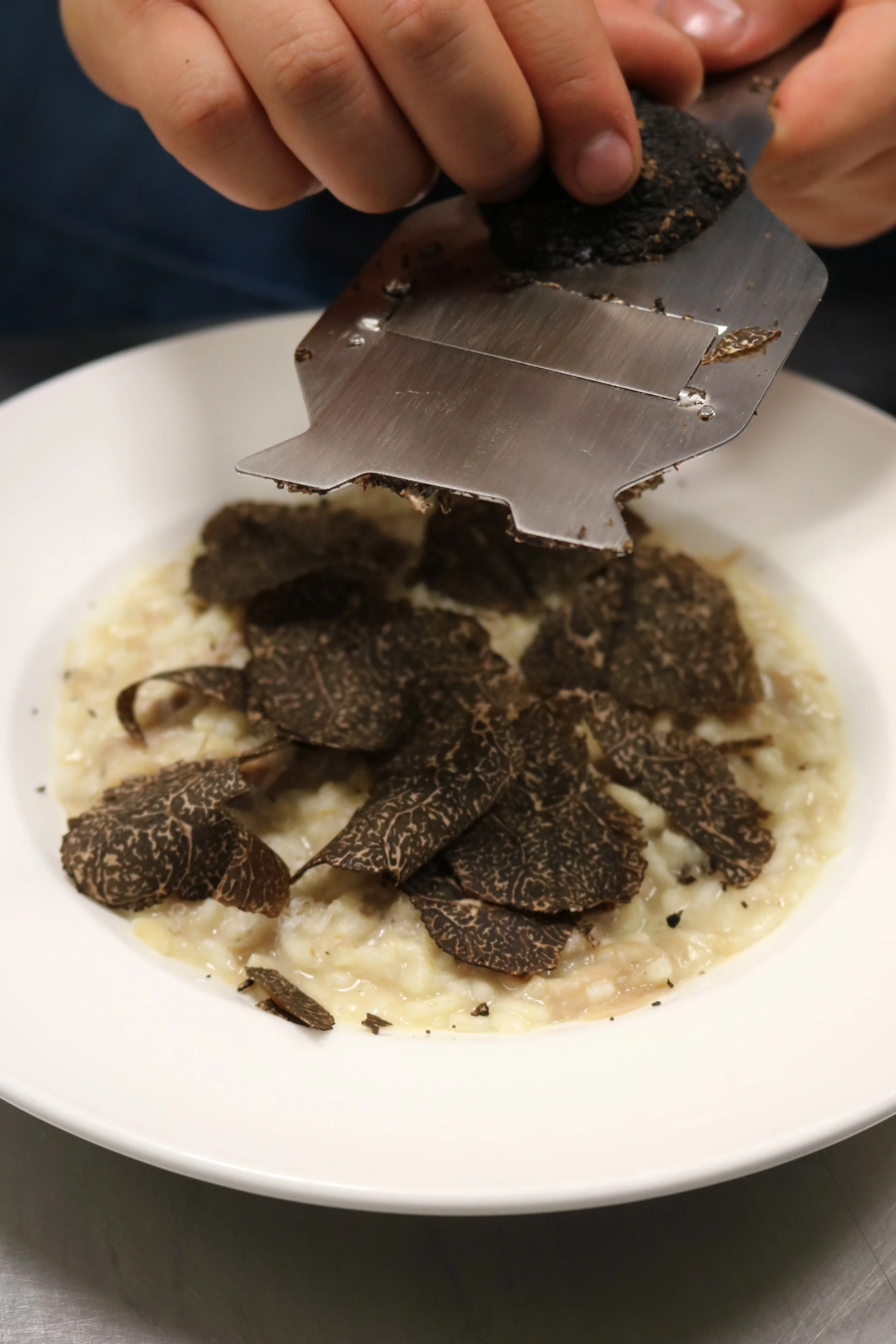 Close-up of black truffles being grated over a bowl of risotto.