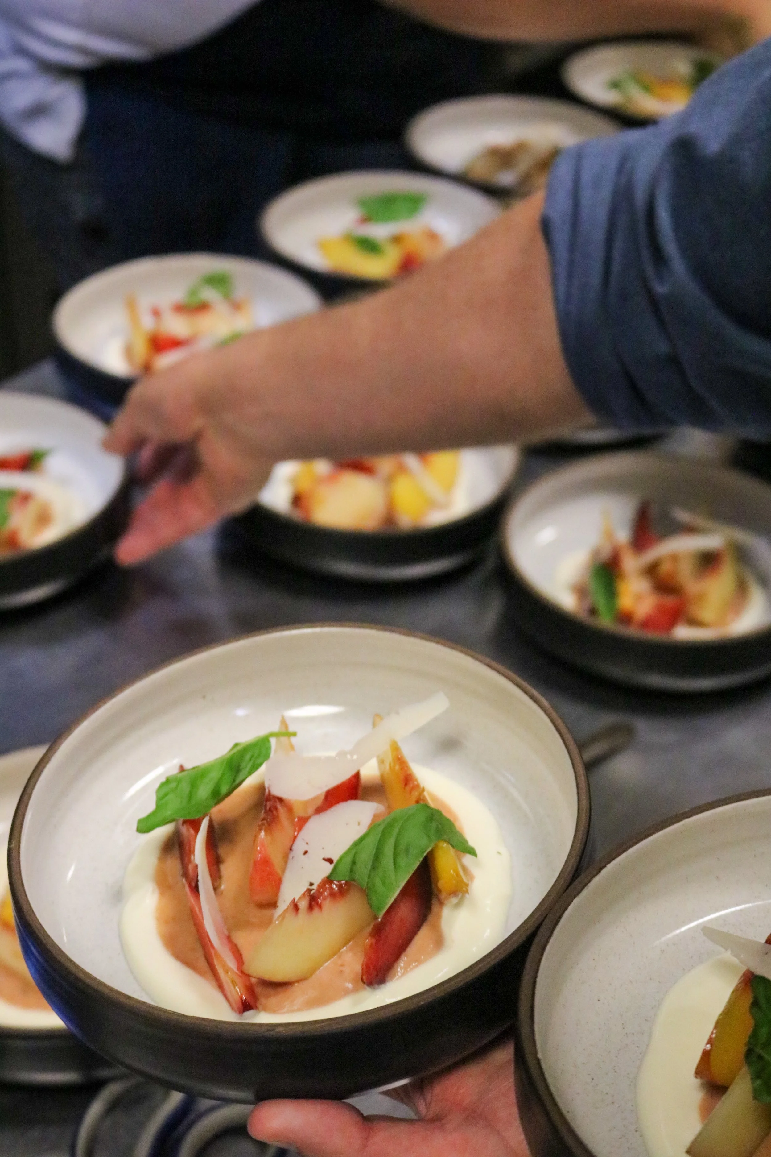 A person holding a small bowl of salad with sliced tomatoes, bell peppers, and fresh basil leaves.