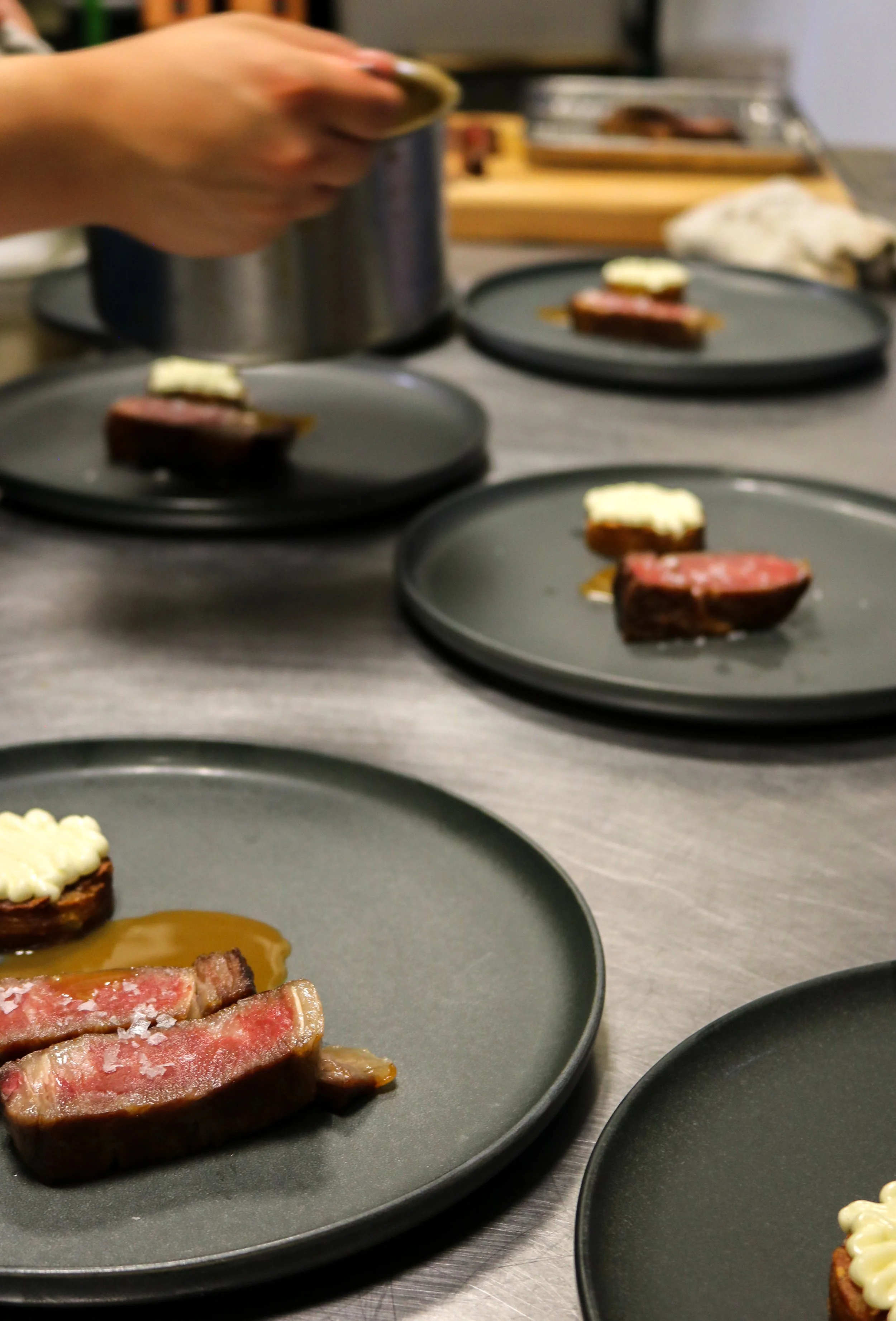 Close-up of plates with raw steaks, some garnished with butter, on a kitchen countertop.