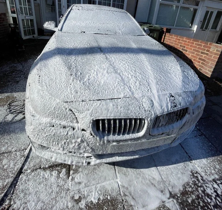 Car covered in soap suds and foam outside on the driveway.