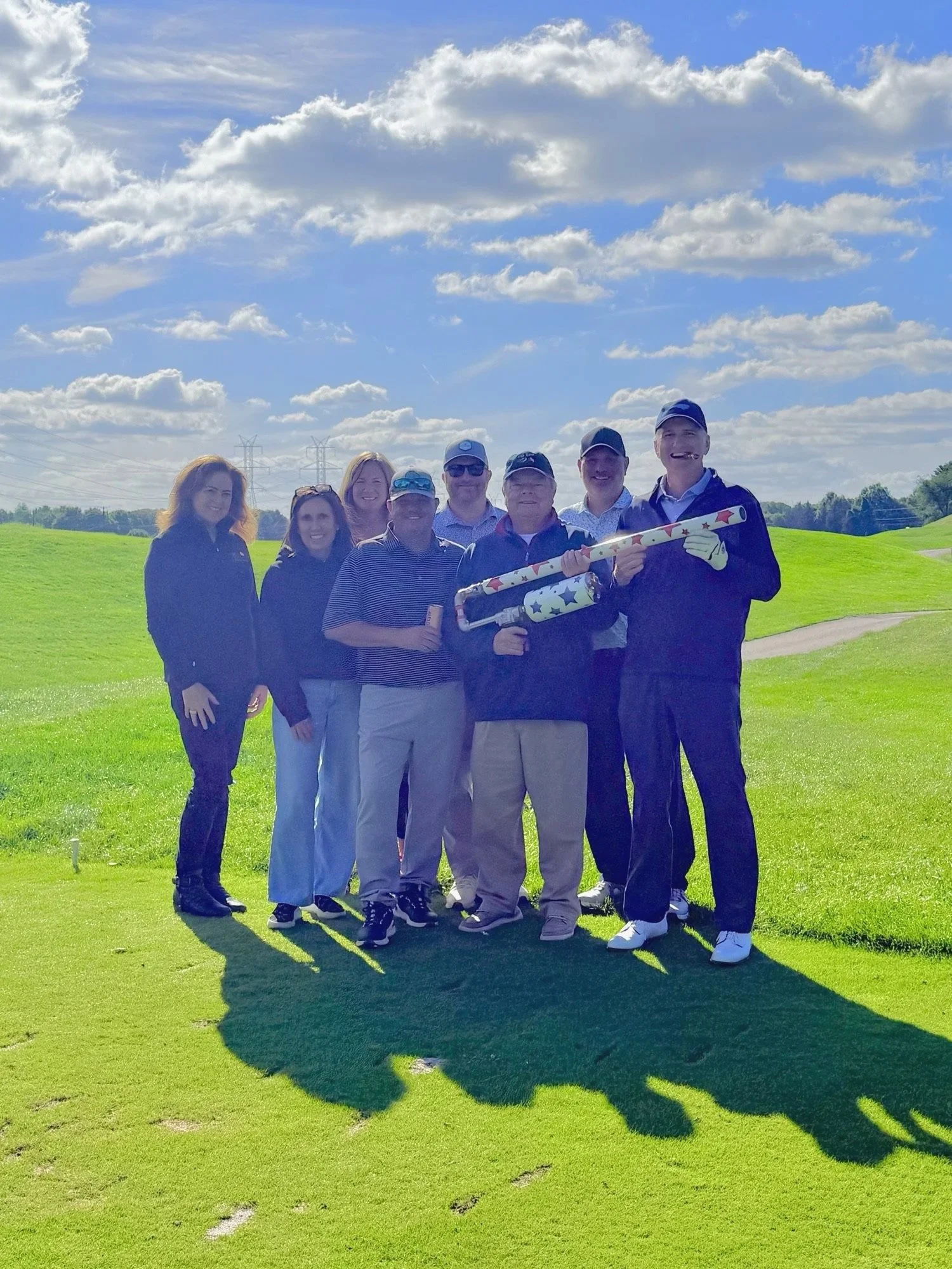 “Seven golfers posing on a Maryland golf course with a golf ball air cannon provided by On Course Experience for charity and corporate golf outings.”