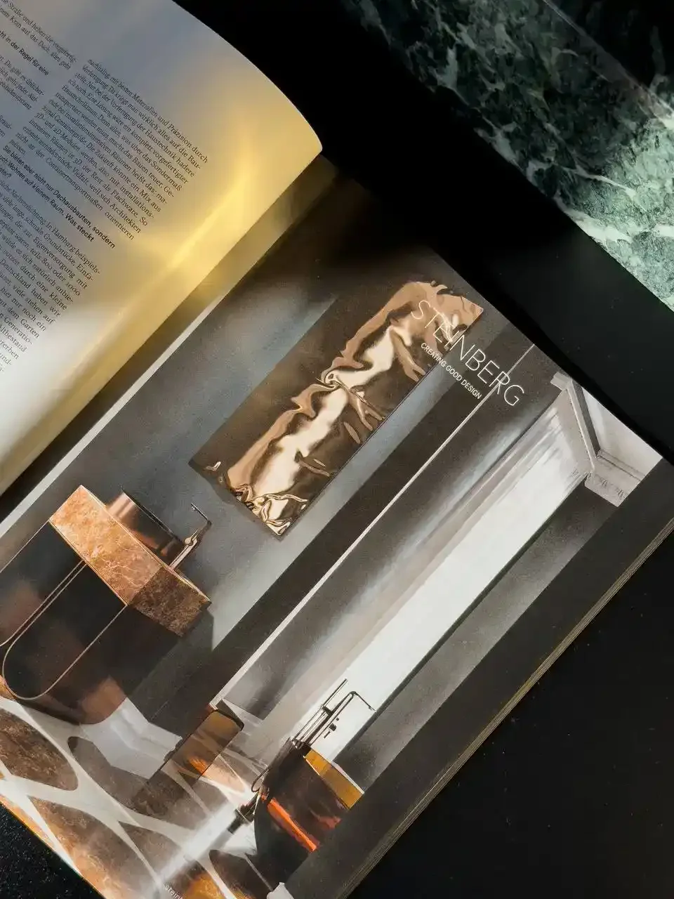Page from an interior design catalog showing a modern bathroom with black and copper fixtures, a dark wall featuring a Marilyn Monroe poster, and a marble countertop with a black sink.