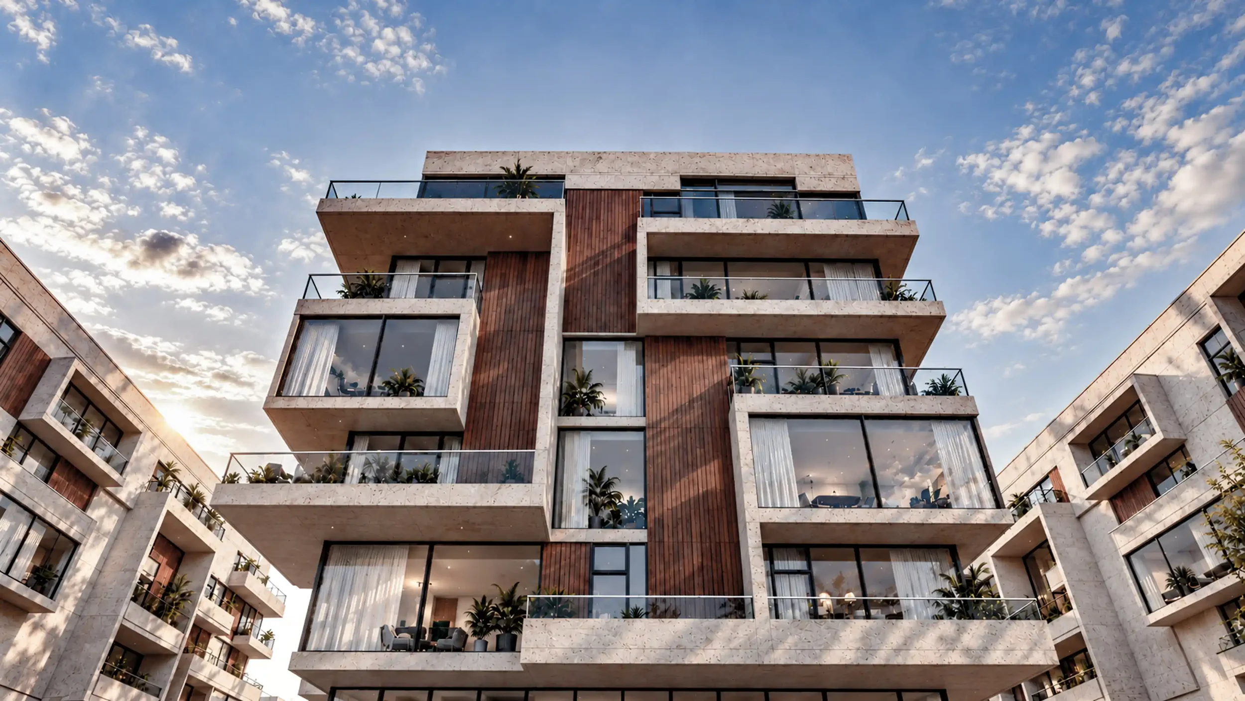 Modern multi-story apartment building with balconies and greenery against a partly cloudy sky at sunset.