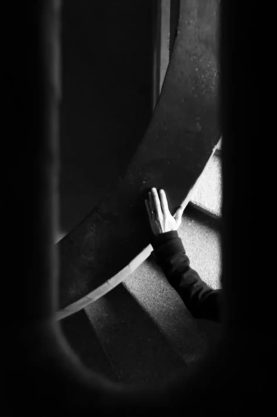 A person's hand touching a large black guitar on a carpeted floor, photographed from above.