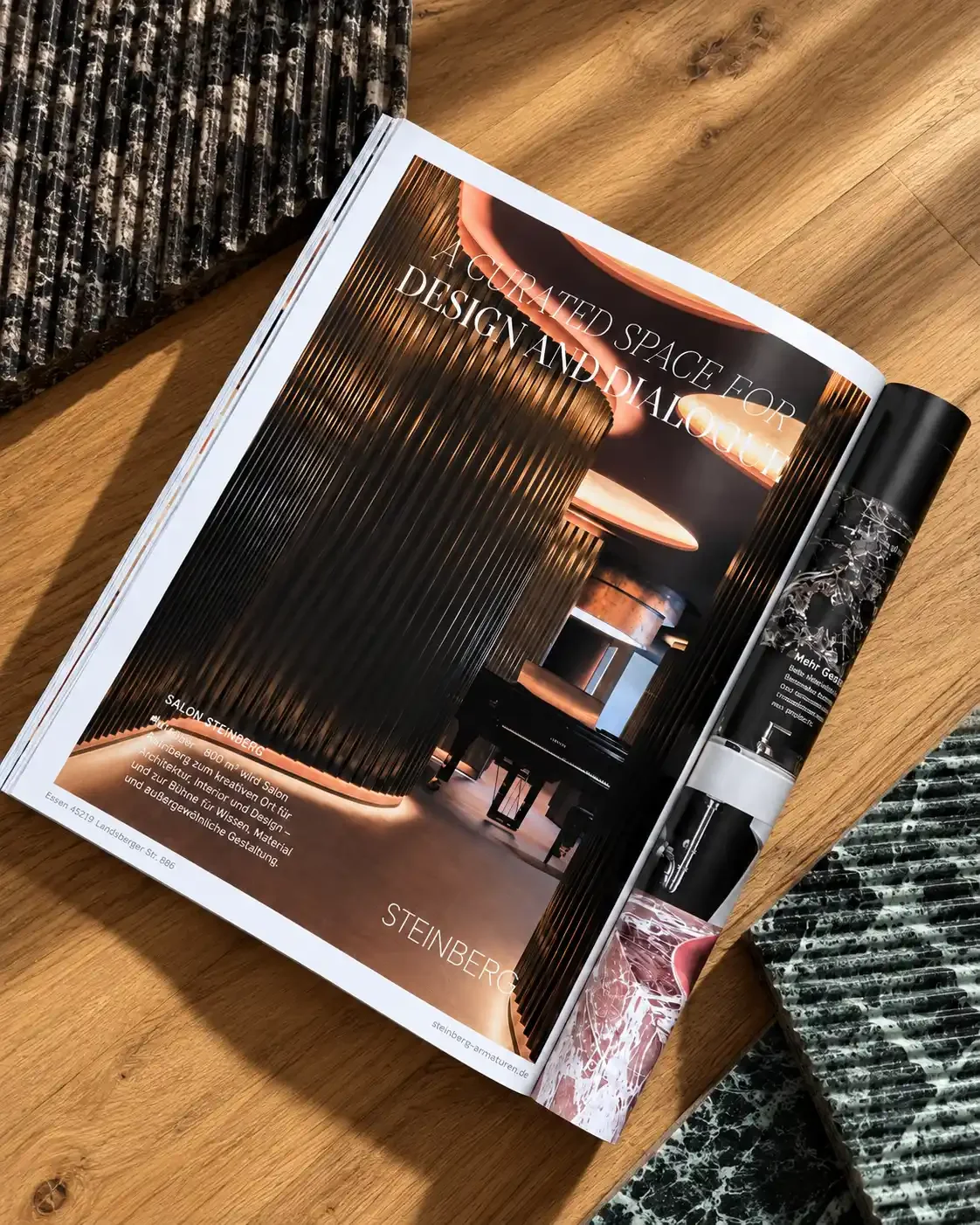 Open magazine on a wooden table showing interior design images and text about a space designed for dialogue, with a black and white patterned vase nearby.
