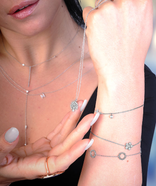 Nahaufnahme einer Frau mit silbernem Schmuck, darunter Halsketten, Armbänder und Ringe, die sie an ihrem Hand- und Handgelenk zeigt.