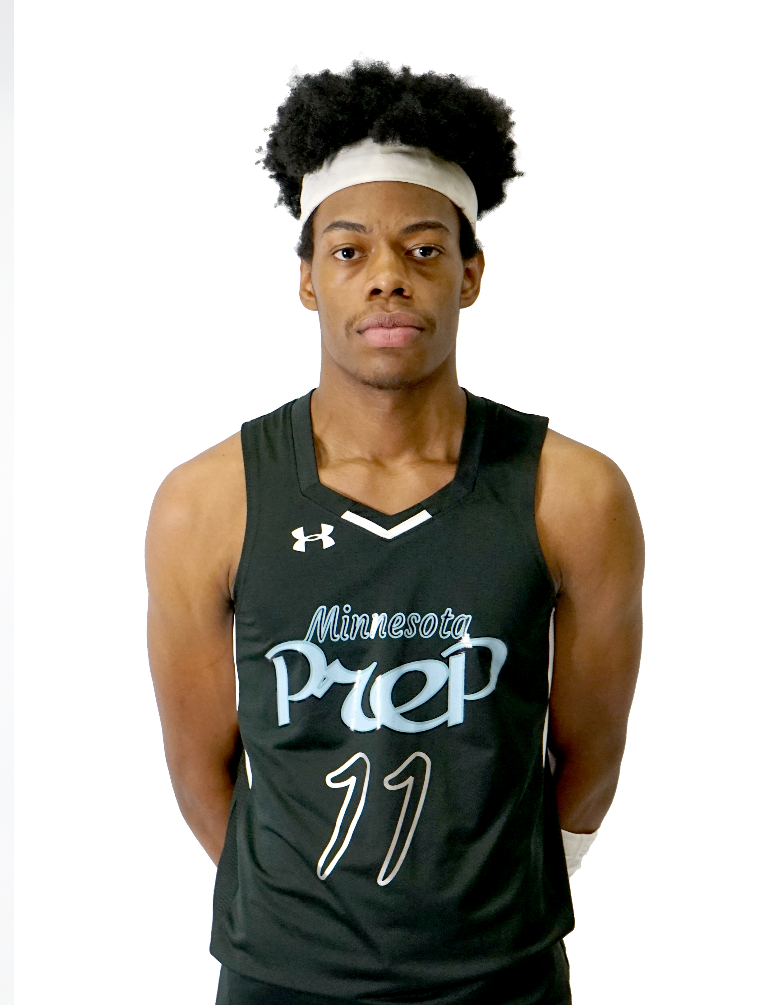 A young man in a black sports jersey with Minnesota Timberwolves written on it and the number 11, standing against a plain white background, wearing a white headband and posing for a photo.