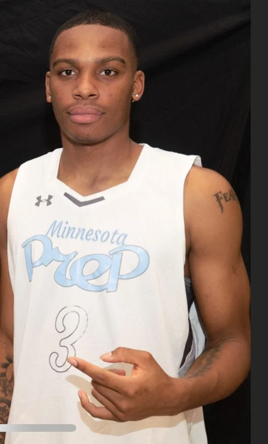 A young man in a Minnesota Prep basketball jersey holds a paper with the number 3 on it, standing against a black backdrop.