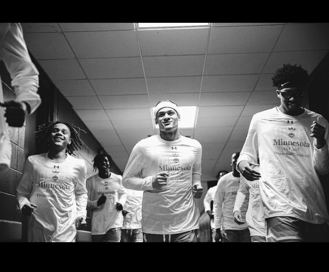 Group of young athletes wearing white Minnesota PREP Academy shirts running together in a corridor.