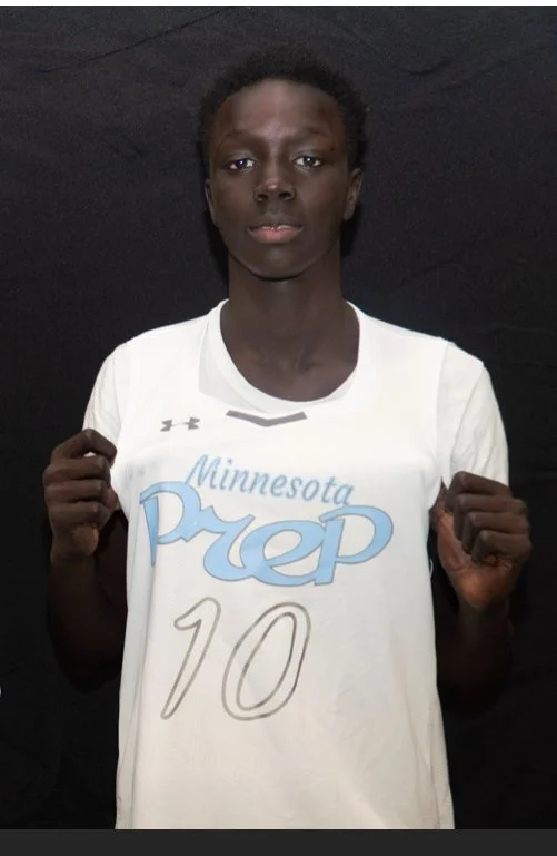 A young man wearing a white sports shirt with the text 'Minnesota Prep' and the number 10, holding his fists up in a gesture of determination or celebration, against a black background.
