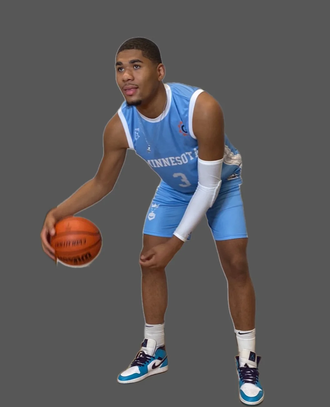 A young male basketball player in a blue Minnesota jersey, holding a basketball, wearing sneakers, standing against a plain gray background.