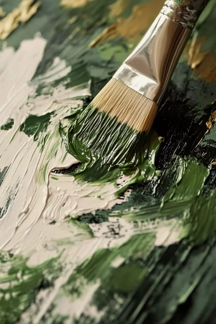 Close-up of a paintbrush applying green and white acrylic paint on a canvas.