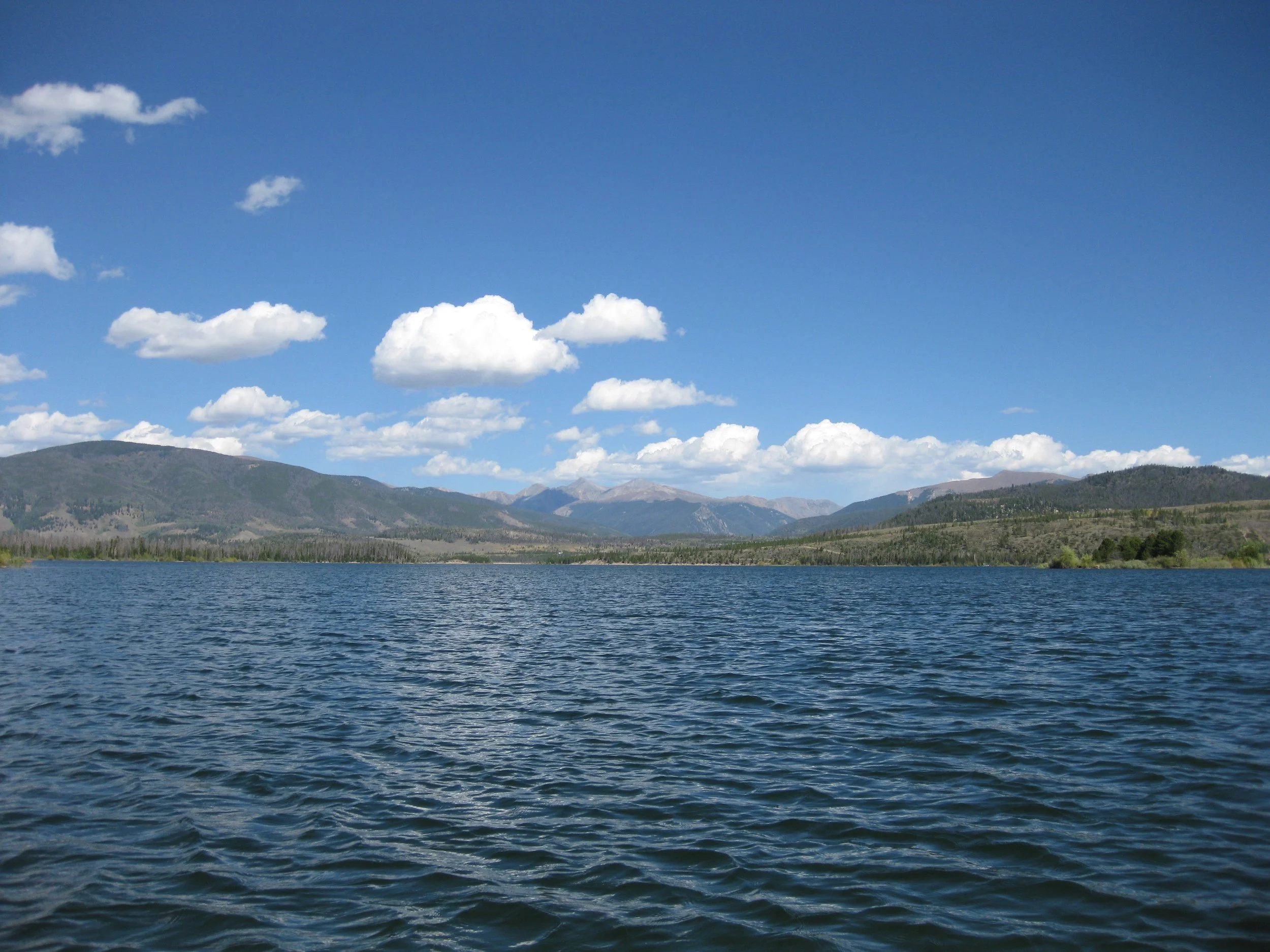 Scenic view of a lake with hills and mountains in the background and a partly cloudy sky overhead.