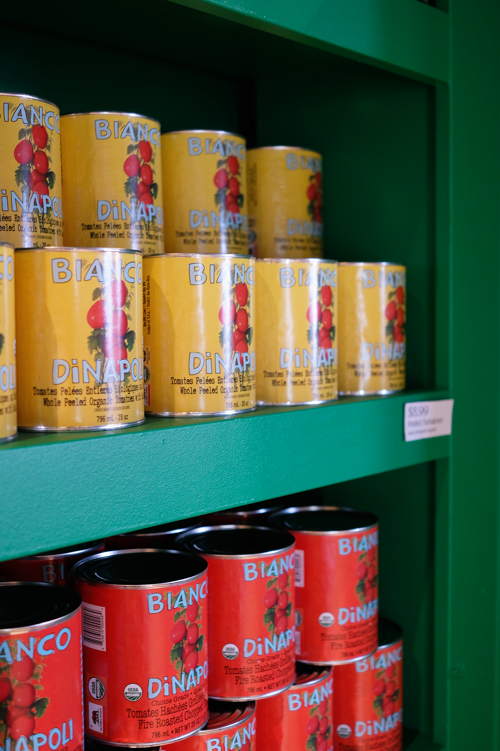 Cans of Bianco D'napoli whole peeled tomatoes on a green shelf.