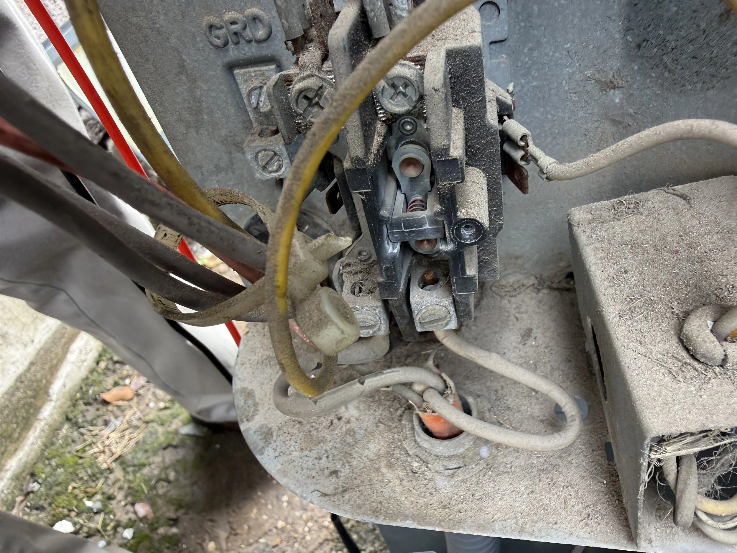 Close-up of a mechanical or electronic component covered in dirt and dust, with several wires surrounding it.