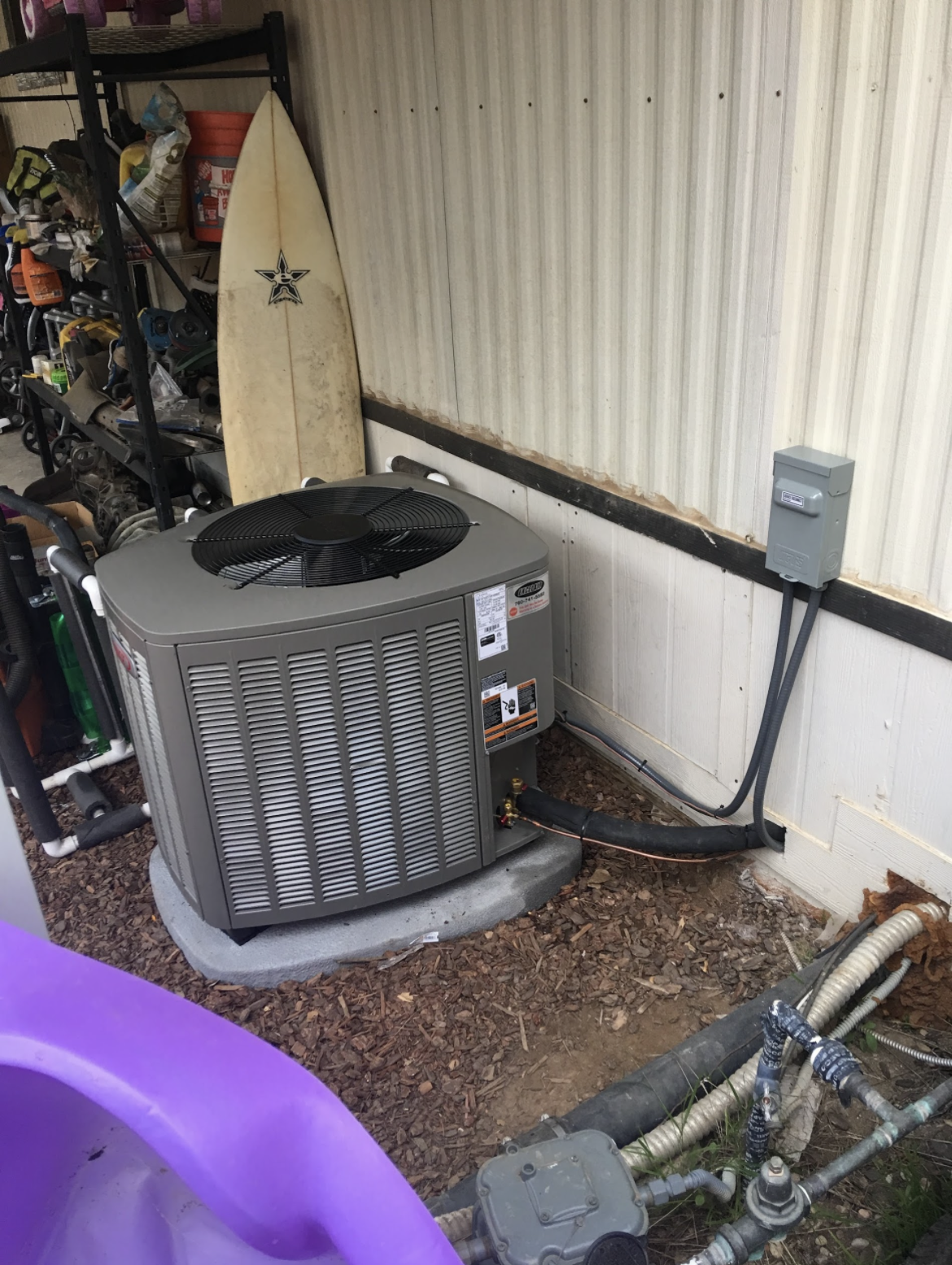 An outdoor air conditioning unit installed beside a house wall with electrical wiring and piping.