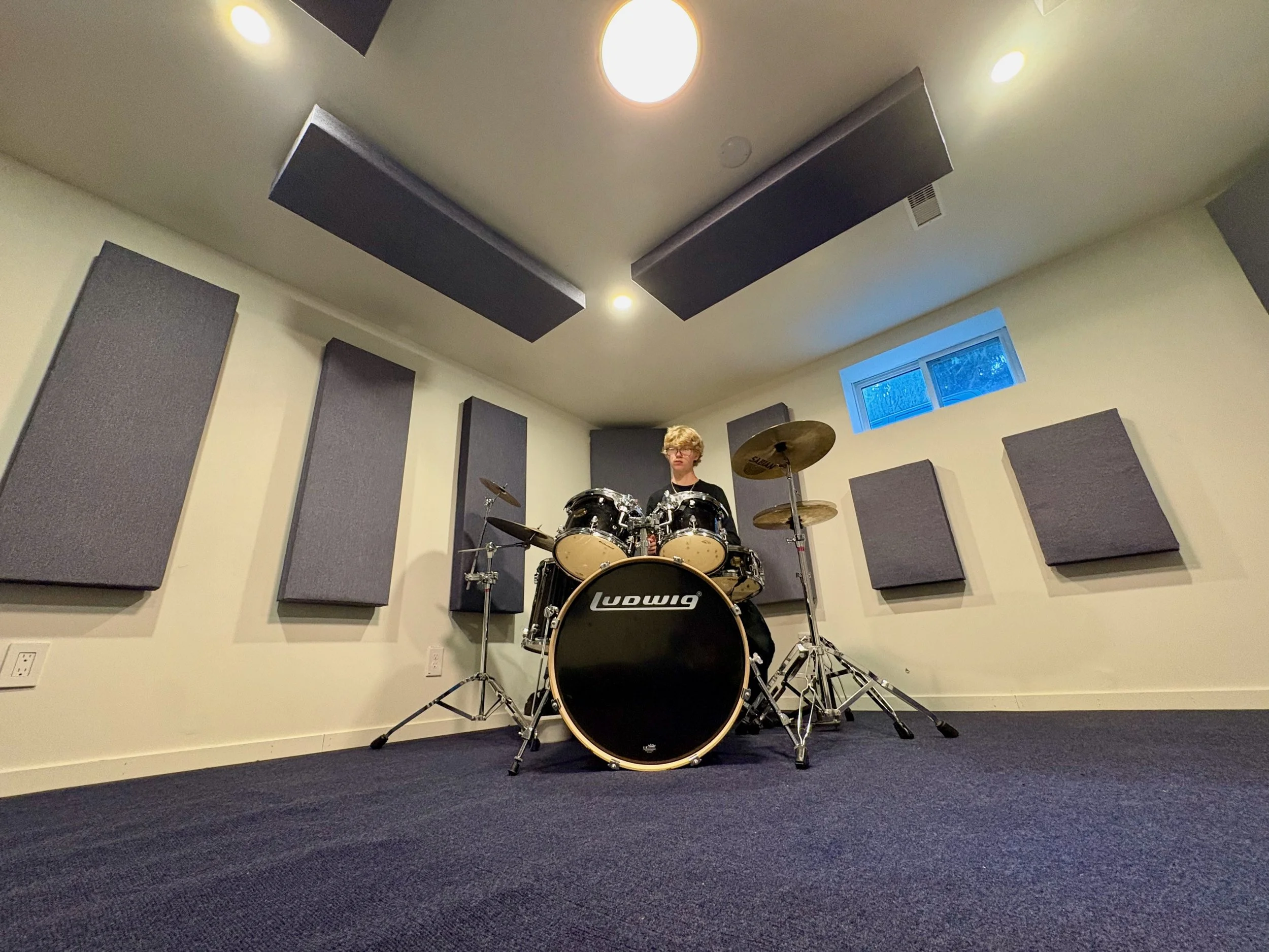 A drummer at his kit in a music room with custom-designed Third Act Acoustics corner bass traps, wall panels and ceiling "clouds".