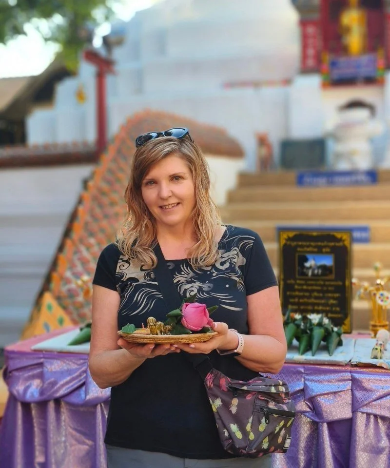 Karen Lantigua, Travel Advisor, smiling and holding a lotus offering in front of a golden temple in Thailand