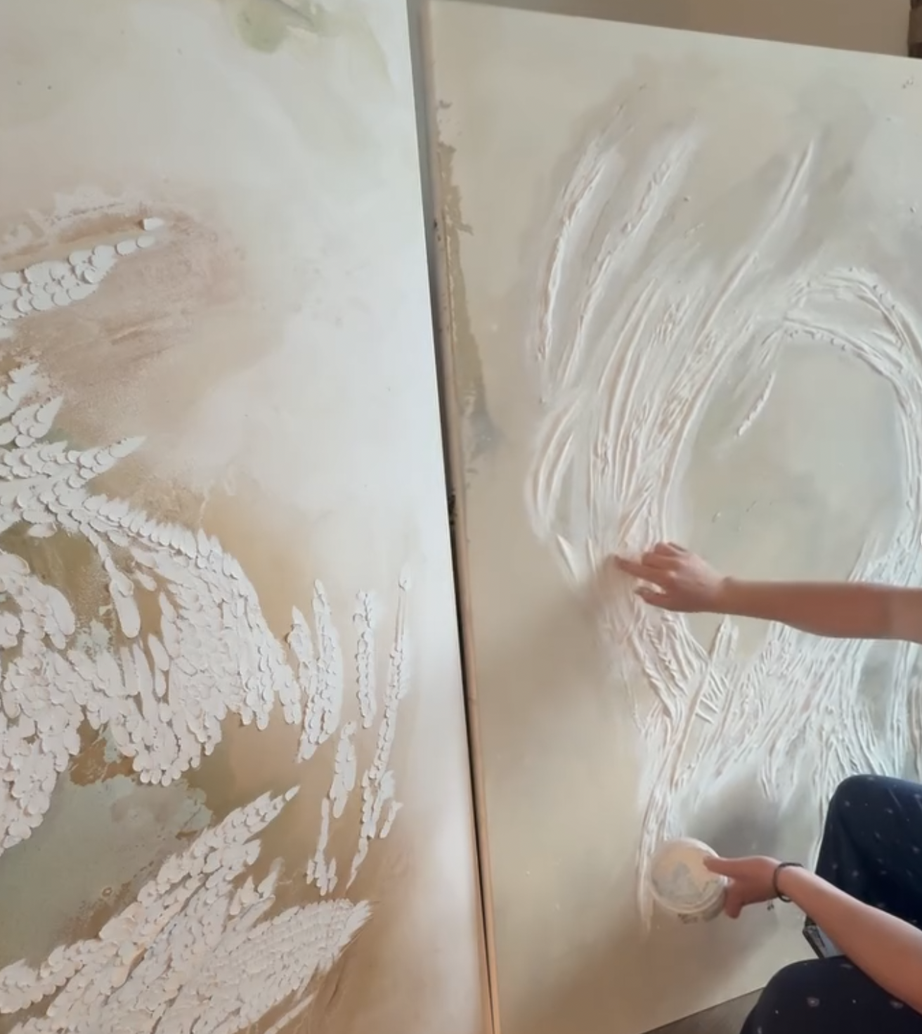 A person creating large, detailed wave paintings on vertically aligned canvases with white textured paint.