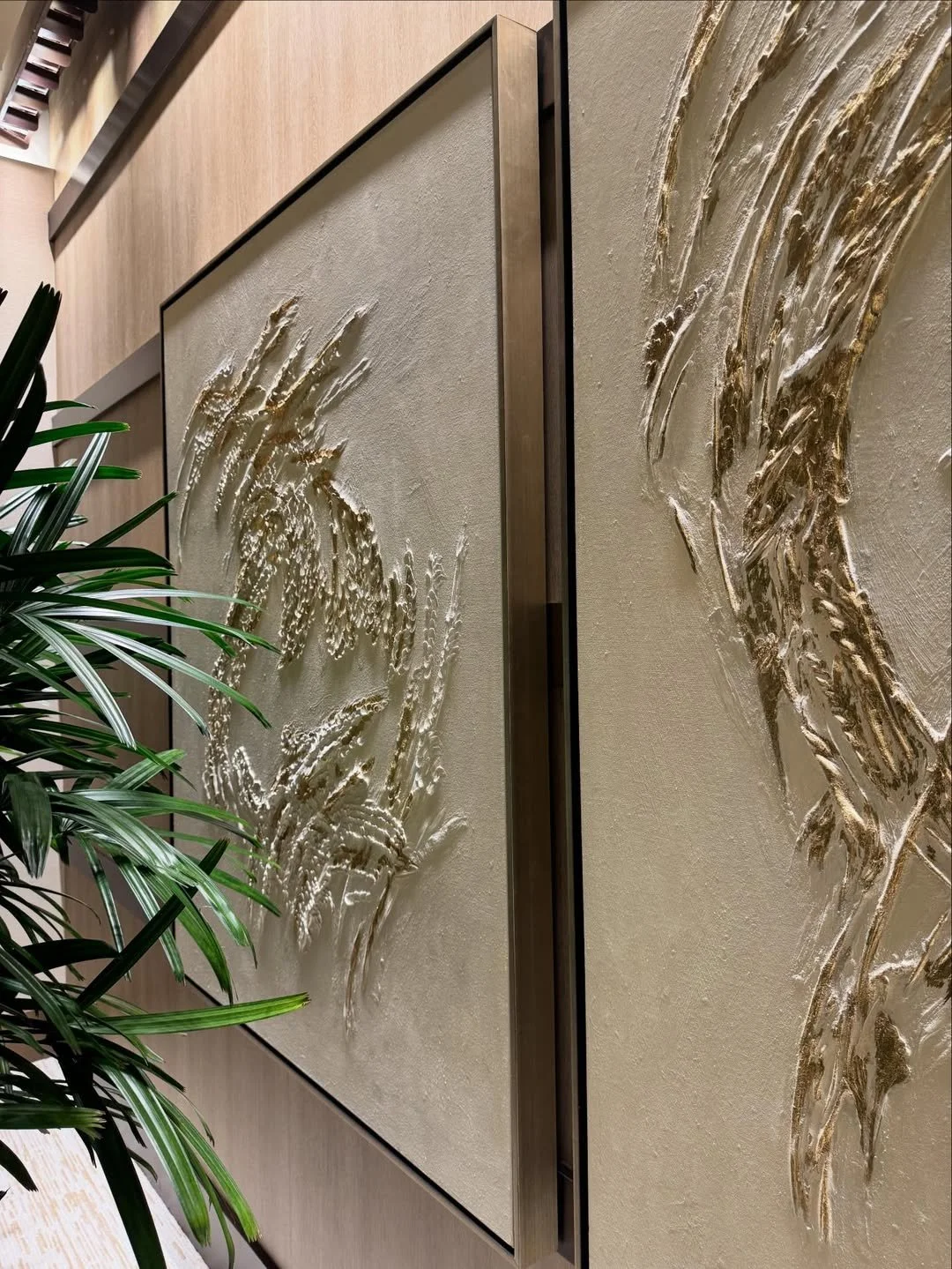 Close-up of a textured wall with a water inspired sculptural design, next to a green plant in an indoor setting.