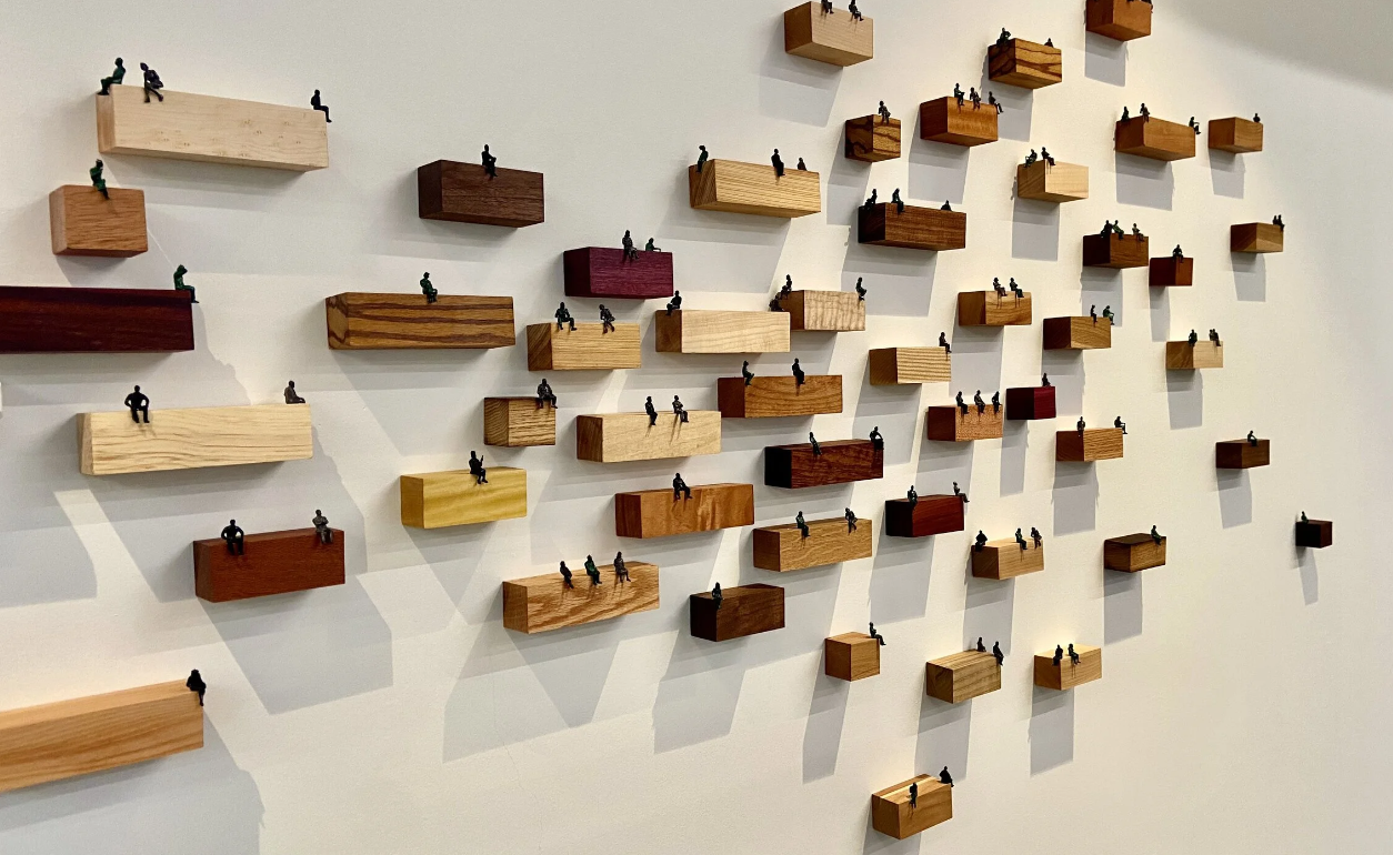 Wooden blocks, cut from wood sold by Olympic Forest Product. Each block  houses small plastic figurines sitting on the edge of each block connecting with one another