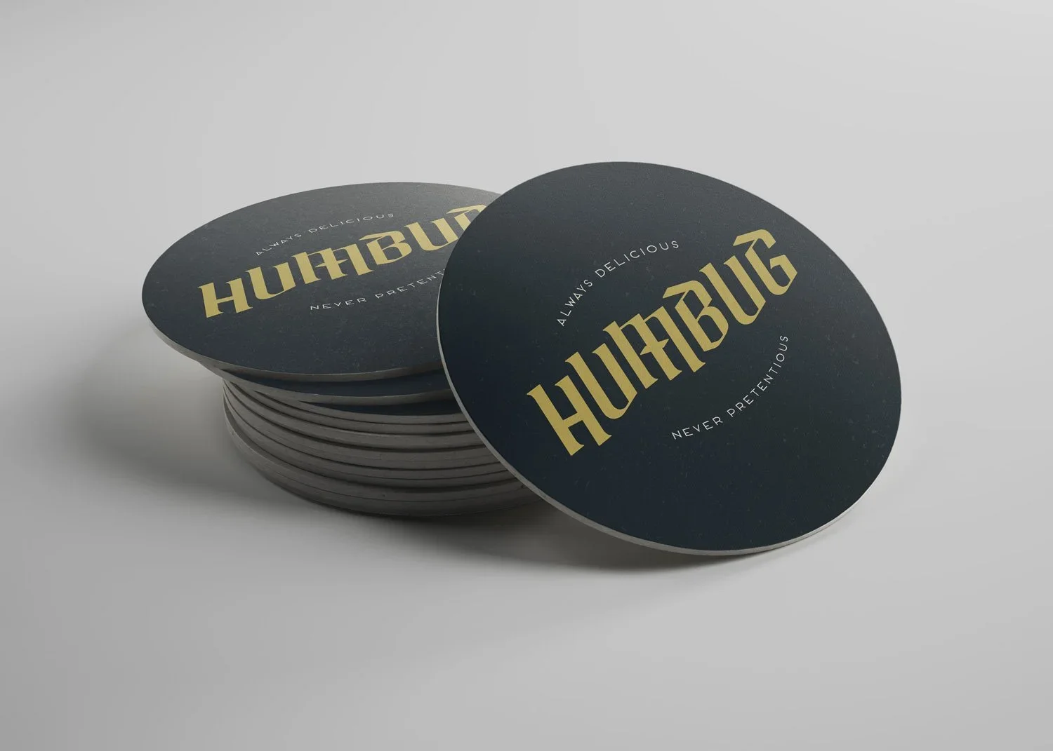 Stack of black HunBun branded drink coasters with gold lettering and white slogans