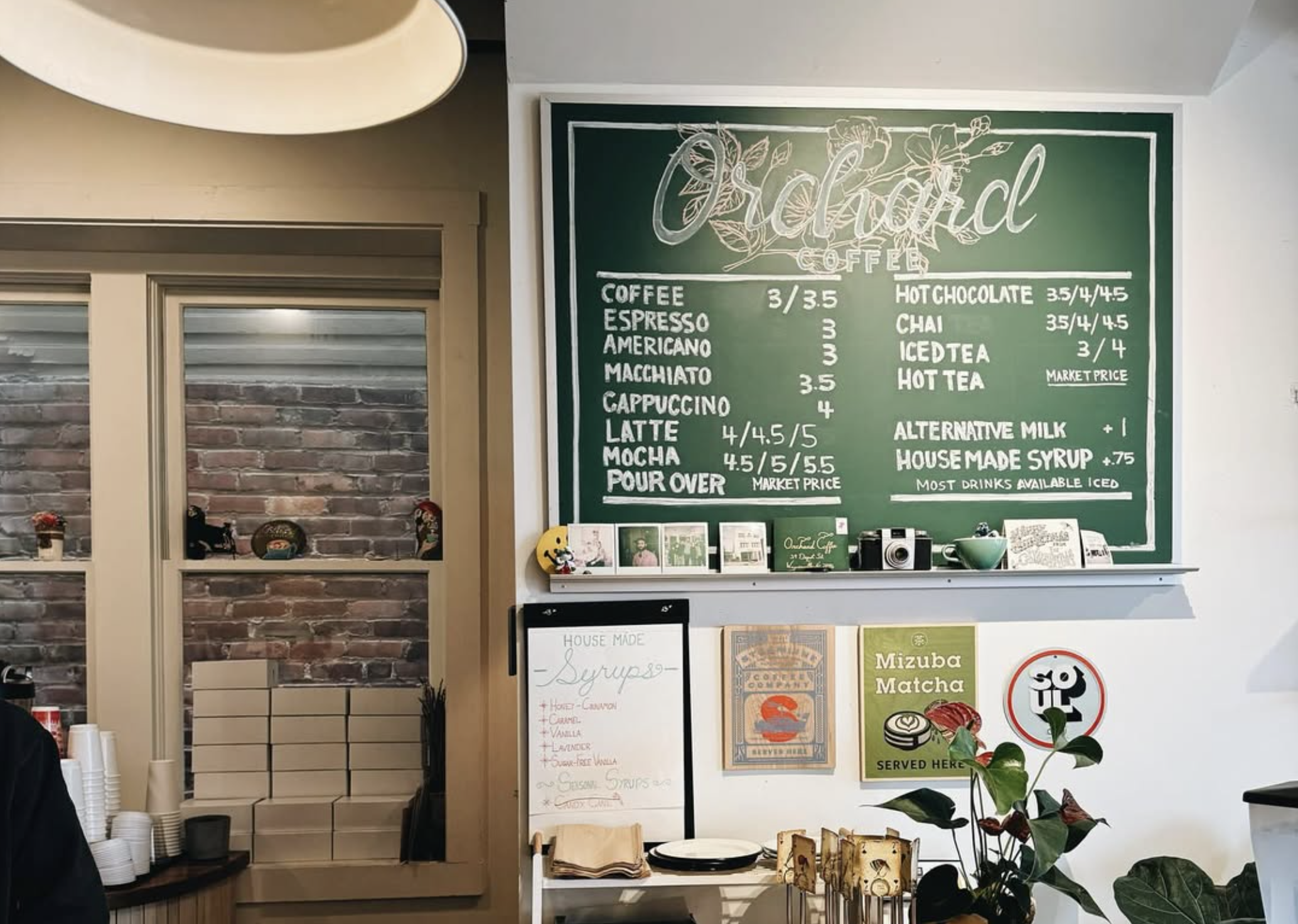 Coffee shop interior with a chalkboard menu listing coffee, espresso, tea, hot chocolate, and specialty drinks above a decorated counter.