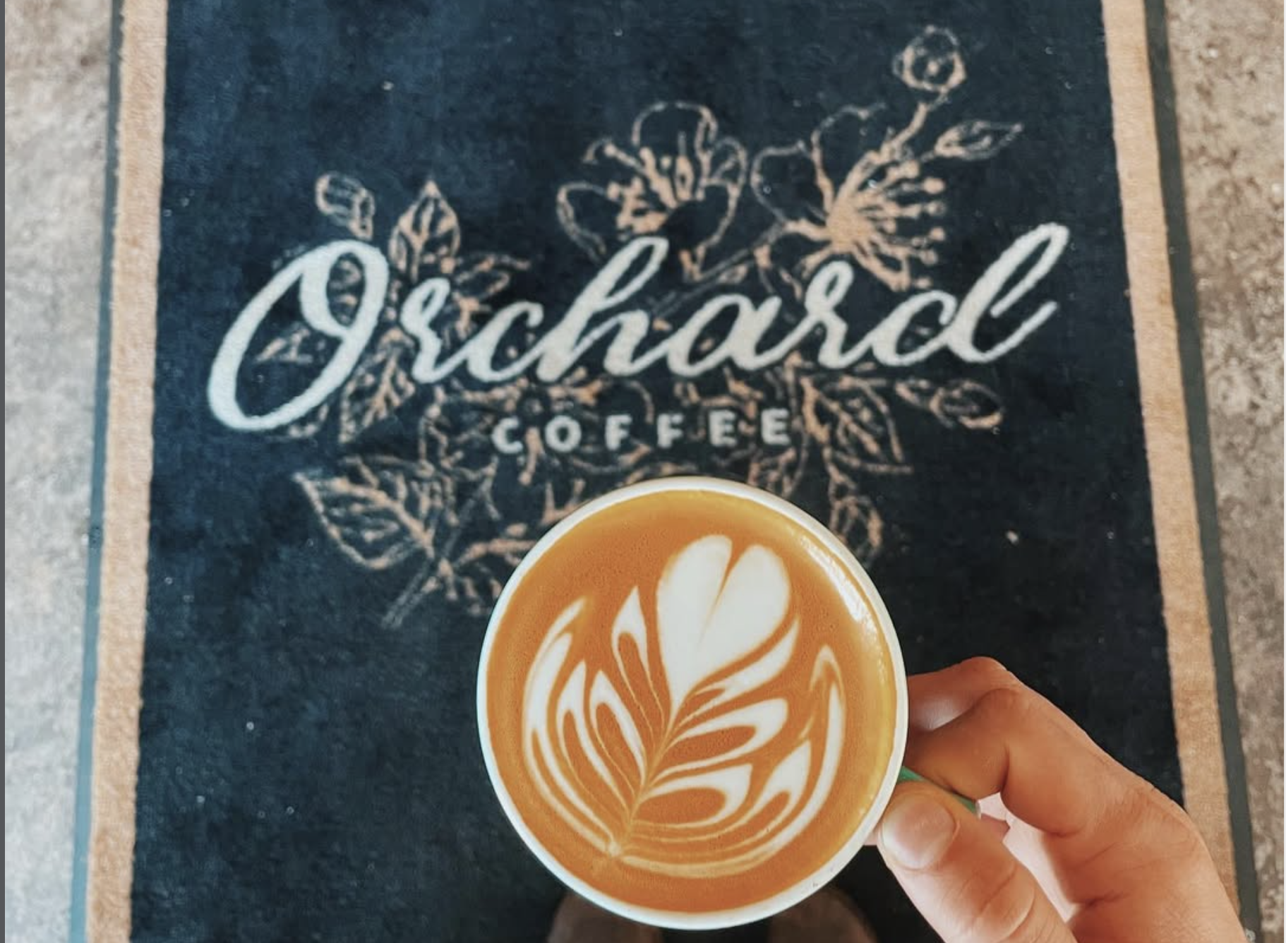 Hand holding a latte with leaf-shaped foam art over a chalkboard reading "Grateful Coffee."