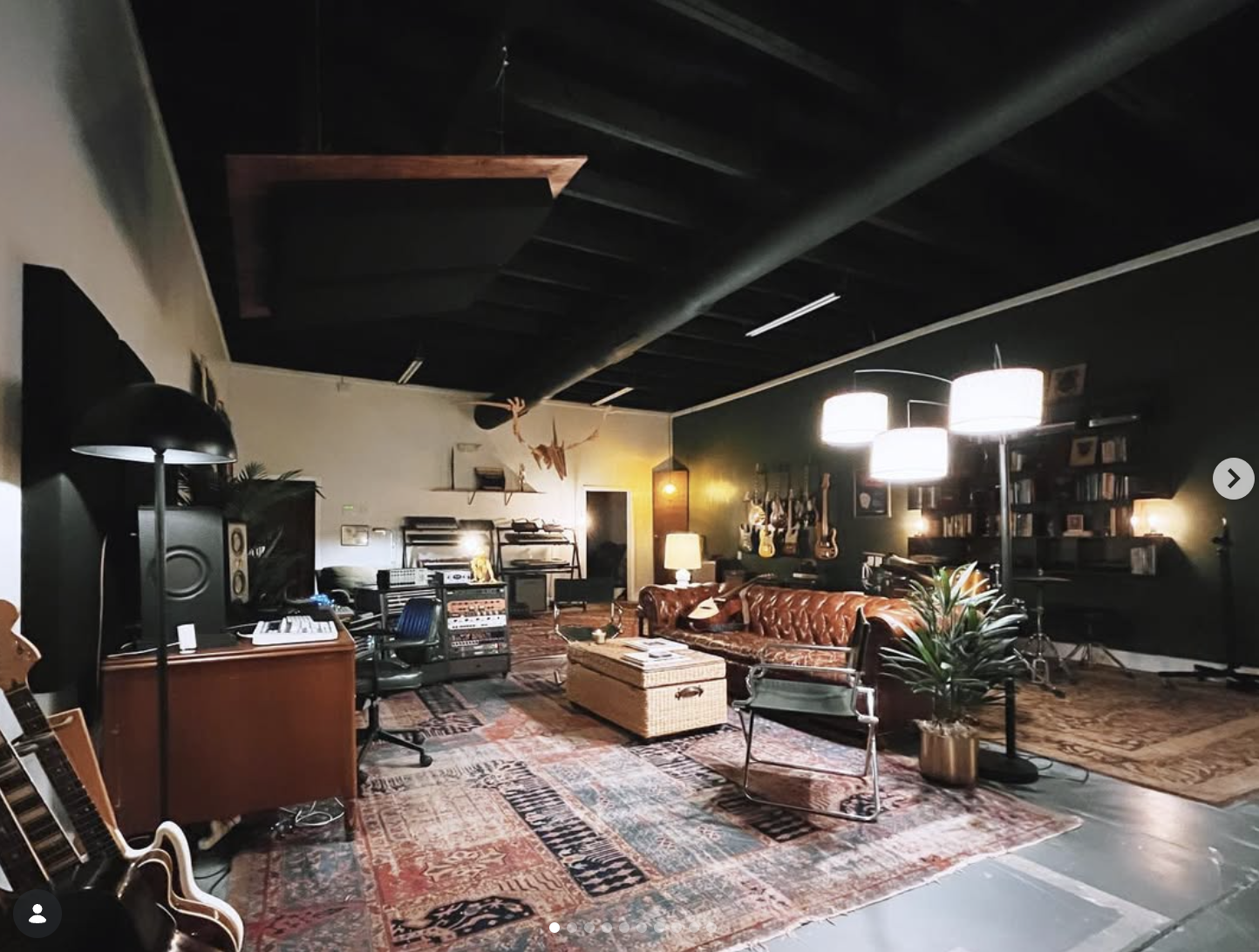 Vintage recording studio lounge with musical instruments, audio equipment, leather sofa, rugs, and guitars on the wall