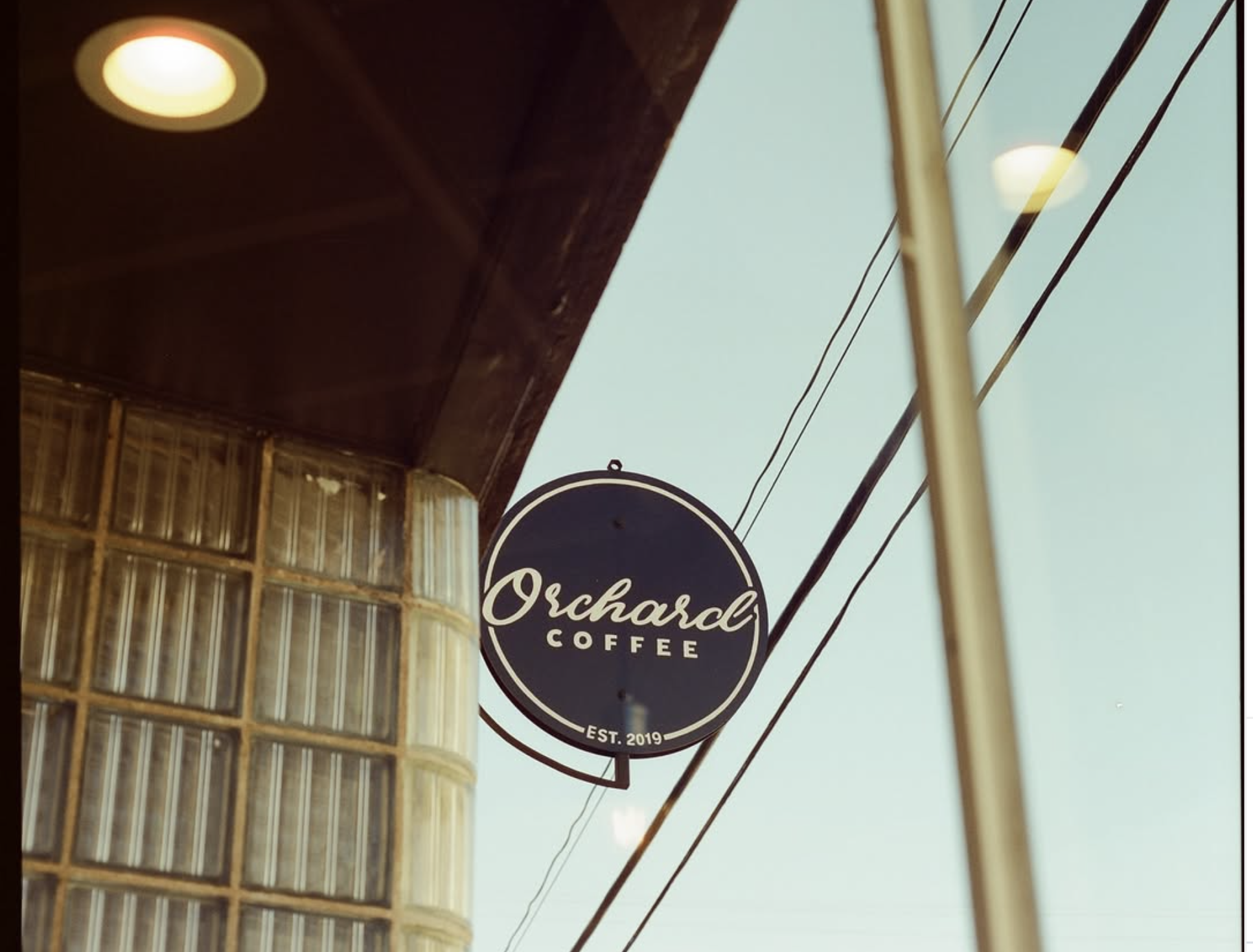 Orchard Coffee storefront sign hanging beneath a covered awning, with utility wires against a blue sky