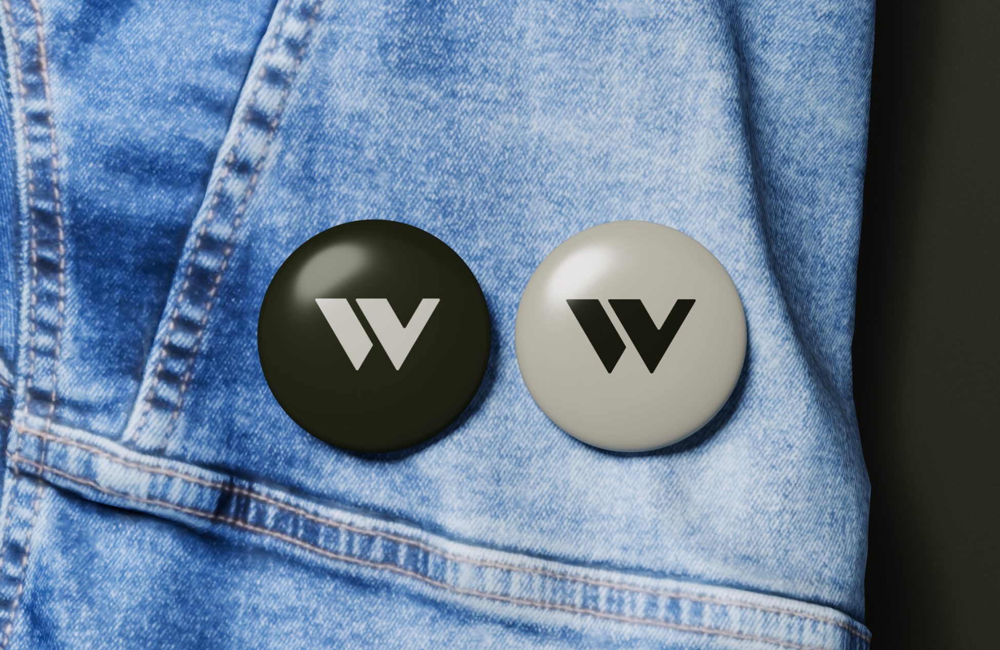 Two round black and white buttons with stylized W logos on blue denim fabric