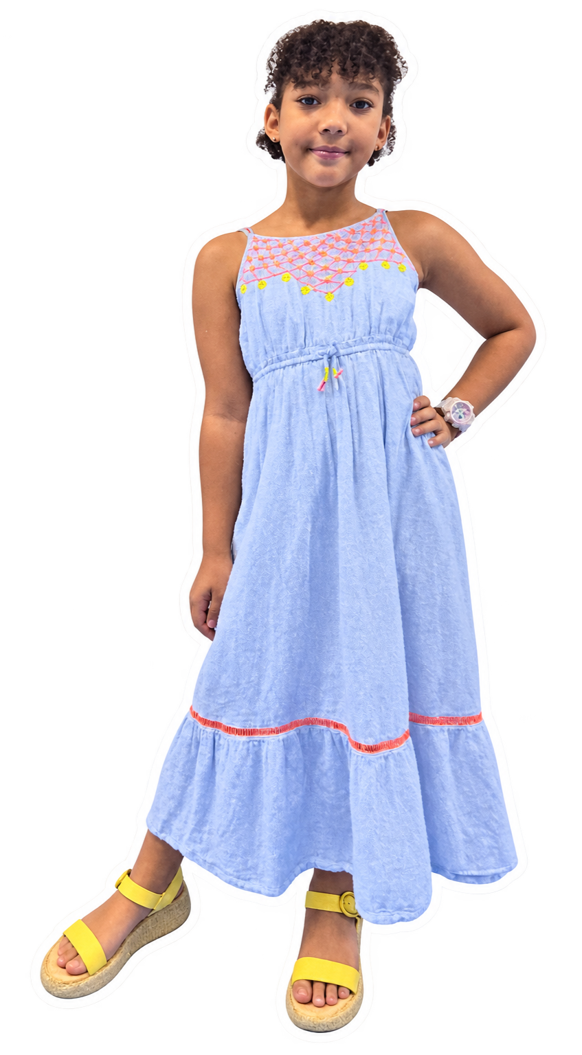 Young girl with curly hair wearing a light blue sleeveless dress with embroidered design near the neckline, yellow accents, a small drawstring at the waist, and a red stripe near the hem. She has a bracelet on her right wrist, yellow sandals, and is standing with one hand on her hip.