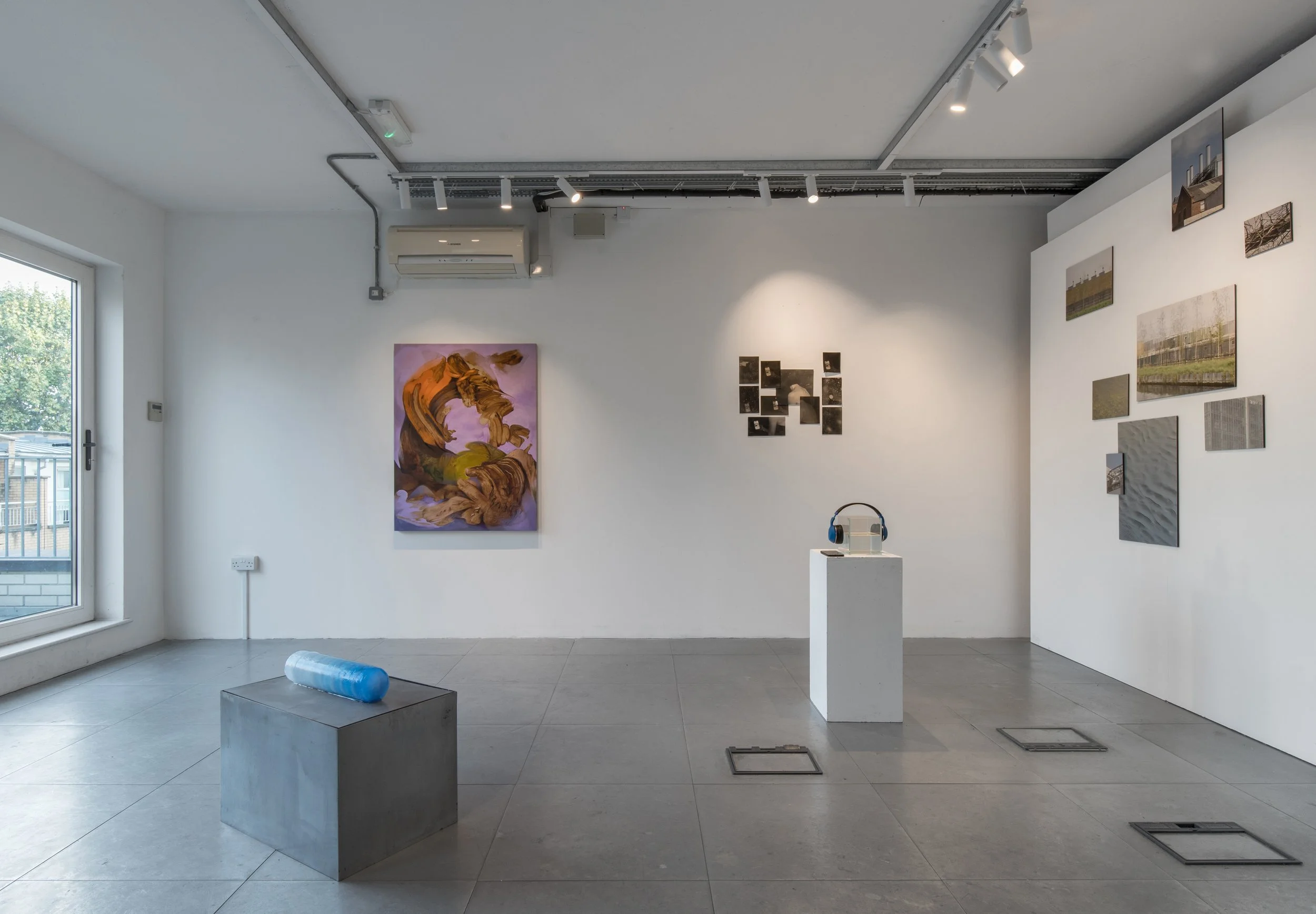 Wide installation view of Commencement / Commandment (2026) at Prokofiev Studio, London, featuring Anastasia Belinskaya's ice-based work Slowest Wave (2026) in the foreground, Kika Sroka-Miller's painting Not drawn from nature (2026) on the central w