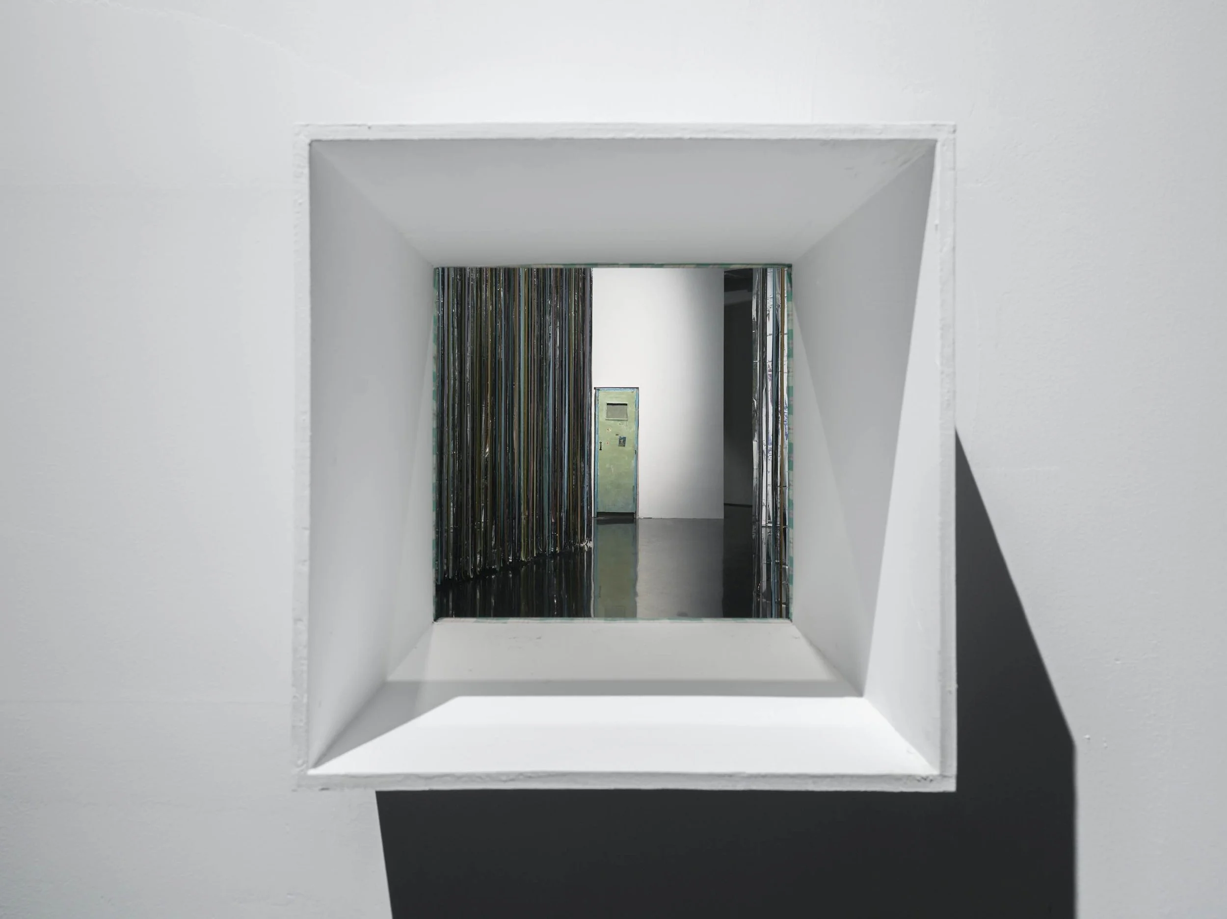 Installation view of Danwei Unfolding (2025) at TANK Shanghai, showing a deep, square architectural opening framing Qiu Xiaofei's weathered green door artwork, with Nishiko's suspended multicoloured ribbons visible in the adjoining gallery space.