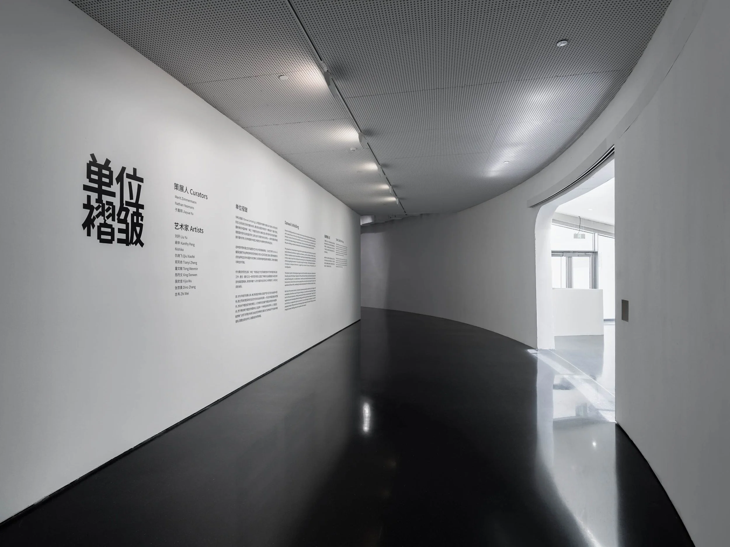 Interior of an art gallery or museum with white curved walls, featuring the gallery text for Danwei Unfolding