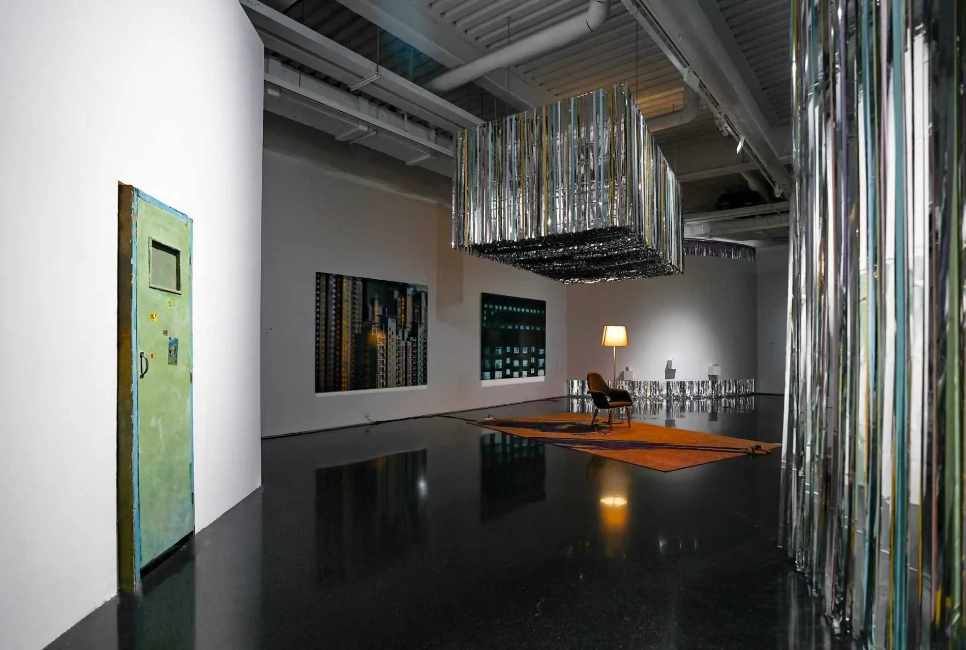 Wide installation view of Danwei Unfolding (2025) at TANK Shanghai, featuring Nishiko's suspended multicoloured ribbons, a green door-like painting by Qiu Xiaofei and Xing Danwen's furnished installation with an orange rug, chair and floor lamp. 
