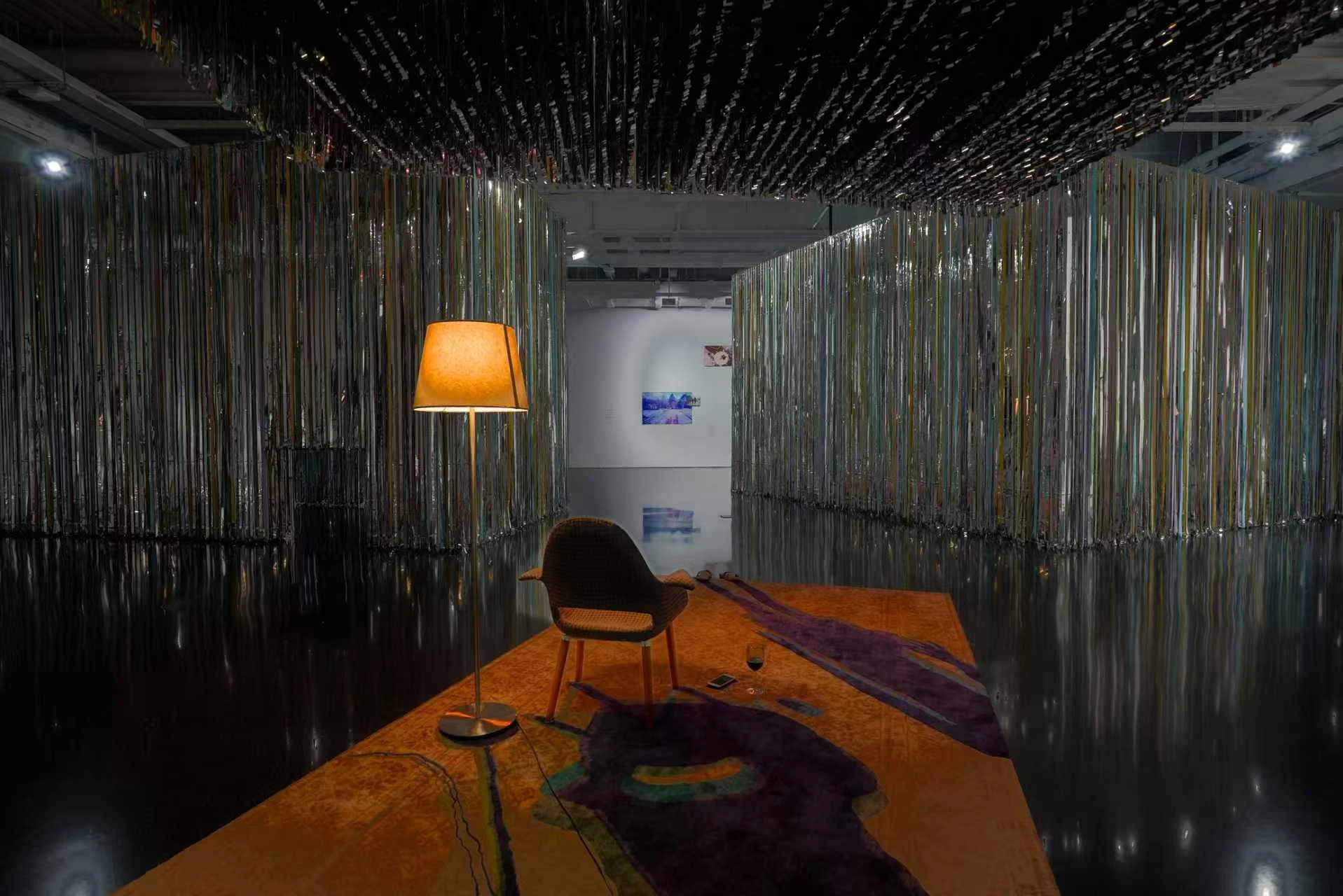 Immersive installation view of Danwei Unfolding (2025) at TANK Shanghai, featuring Xing Danwen's furnished interior with an orange rug, chair and illuminated floor lamp, surrounded by Nishiko's suspended multicoloured ribbons.