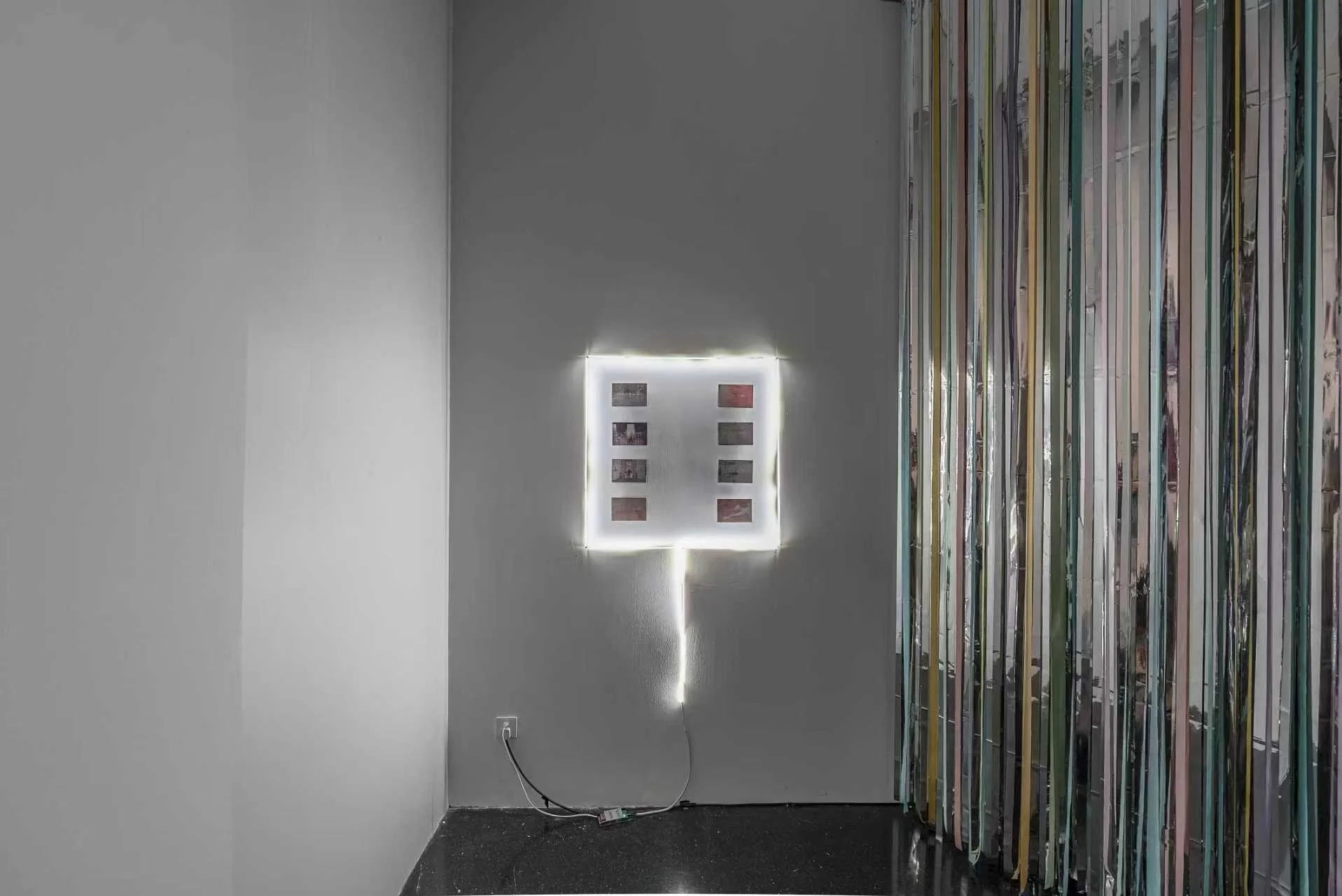 Installation view of an illuminated photographic work by Zheng Tianyi in Danwei Unfolding (2025) at TANK Shanghai, featuring a grid of eight photographs framed by white light, with Nishiko's suspended multicoloured ribbons visible to the right.