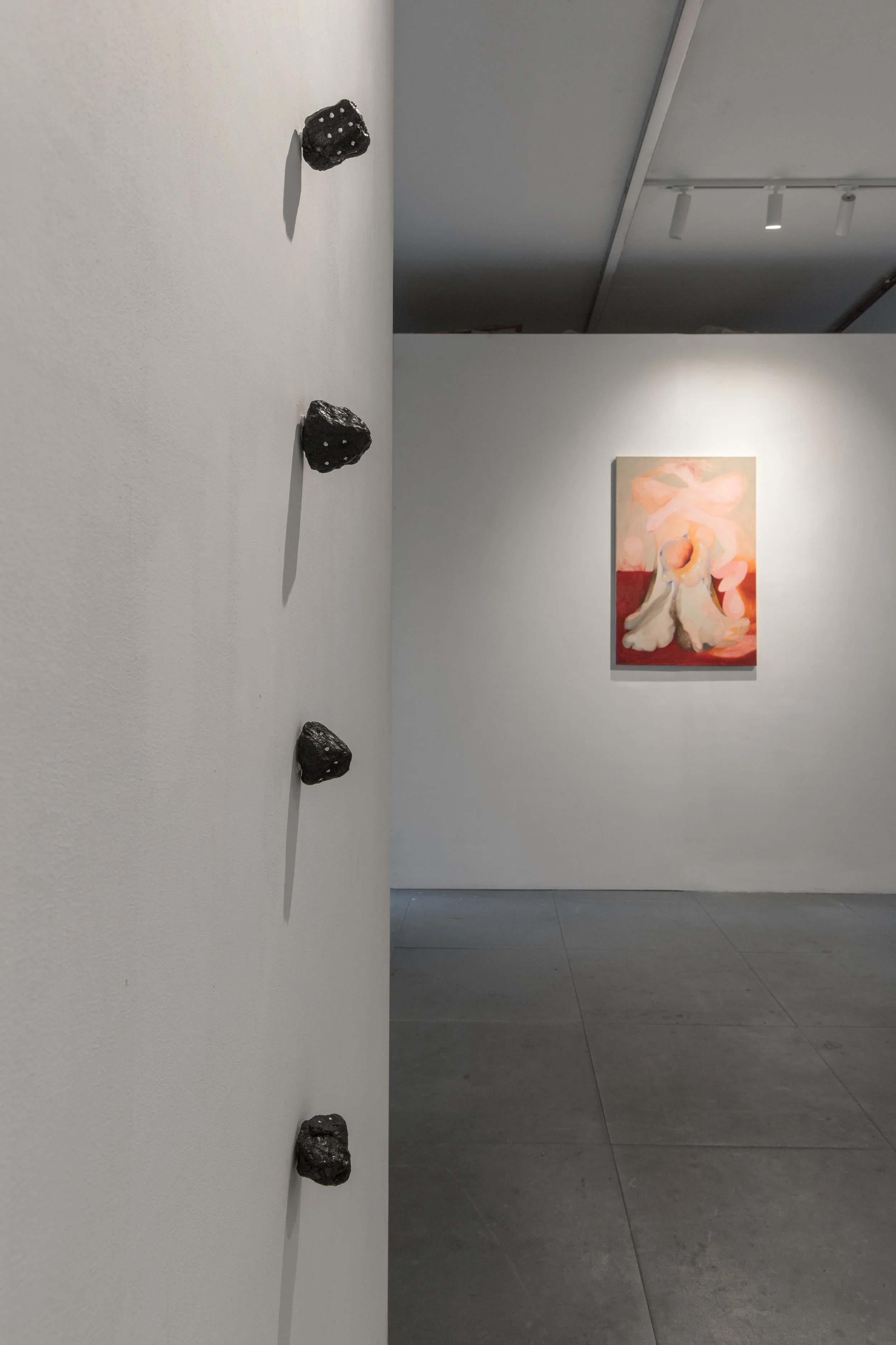 Installation view of Commencement / Commandment (2026) at Prokofiev Studio, London, featuring Anastasia Belinskaya's Dice (2024), a series of small dark sculptural forms mounted along the foreground wall, with Kika Sroka-Miller's painting You are fre