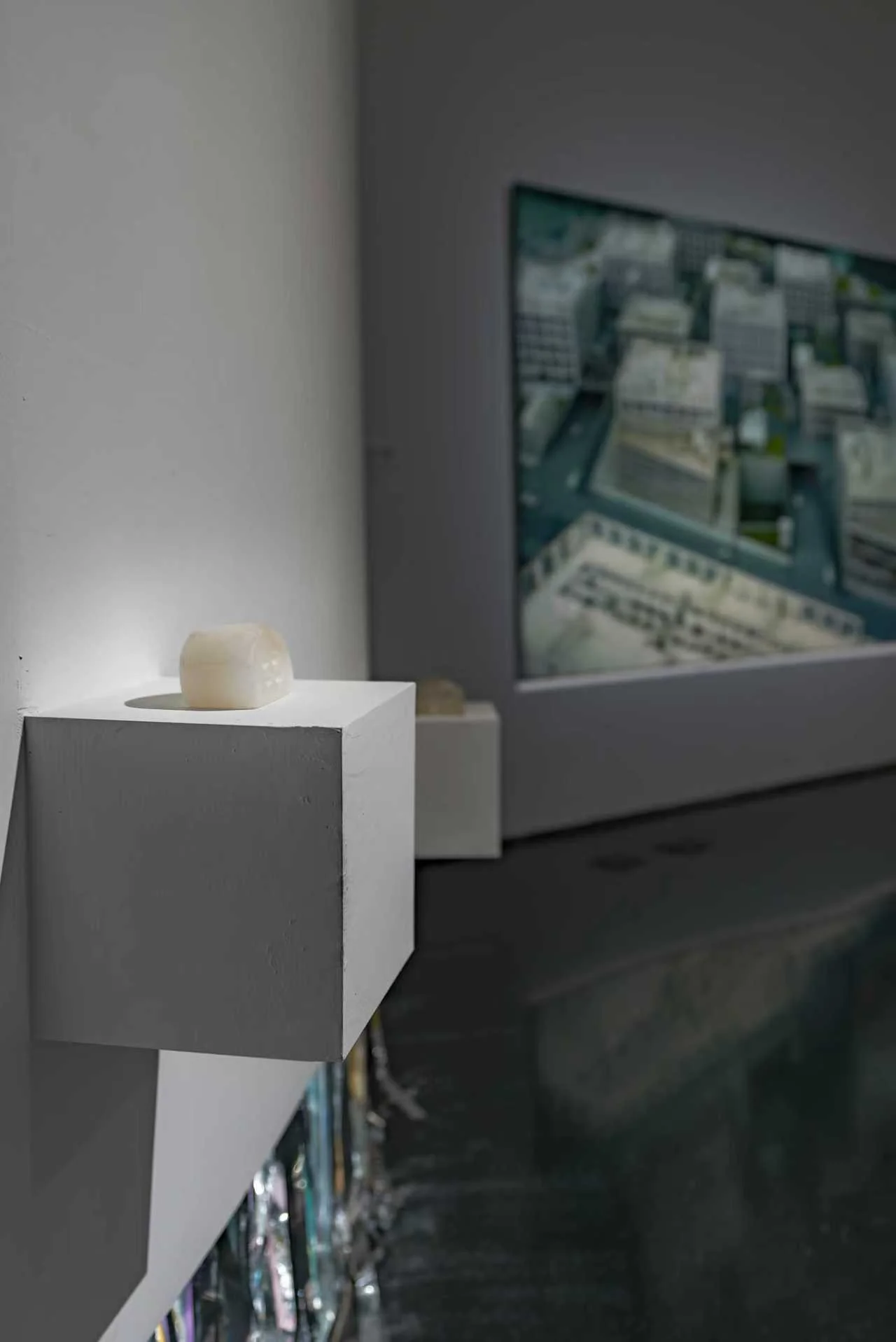 Installation view of a small, pale sculptural work by Yijia displayed on a white wall-mounted plinth in Danwei Unfolding (2025) at TANK Shanghai, with Xing Danwen's photographic work visible in the background.