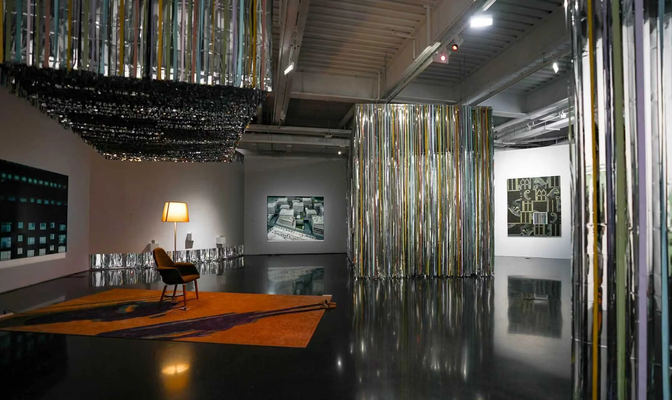 Installation view of Danwei Unfolding (2025) at TANK Shanghai, featuring an orange rug, chair and floor lamp within Xing Danwen's installation, surrounded by Nishiko's suspended multicoloured ribbons, with Zhi Wei's Puzzle Piece visible on the right-