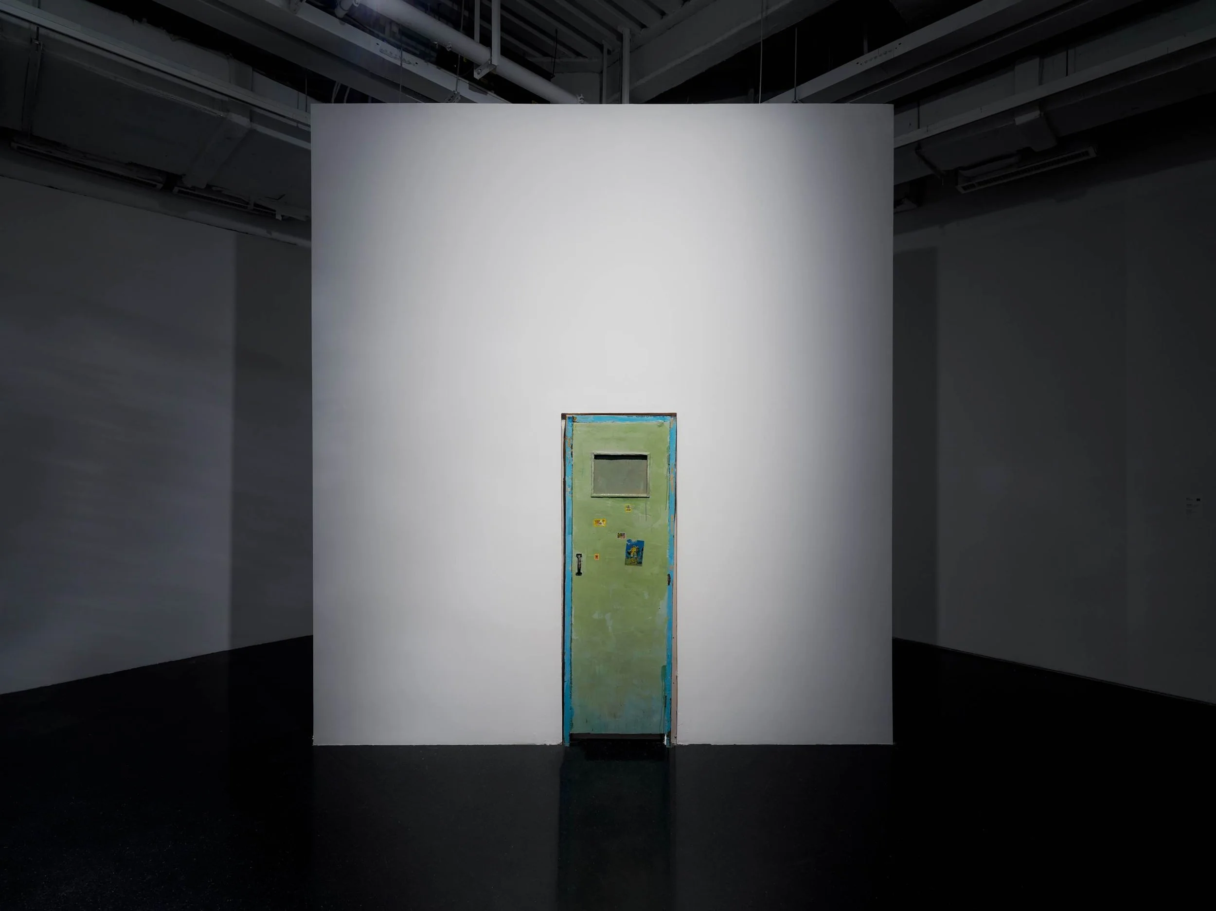 Installation view of a weathered green door artwork by Qiu Xiaofei in Danwei Unfolding (2025) at TANK Shanghai, featuring a narrow rectangular window and small coloured details, displayed against a freestanding white gallery wall.