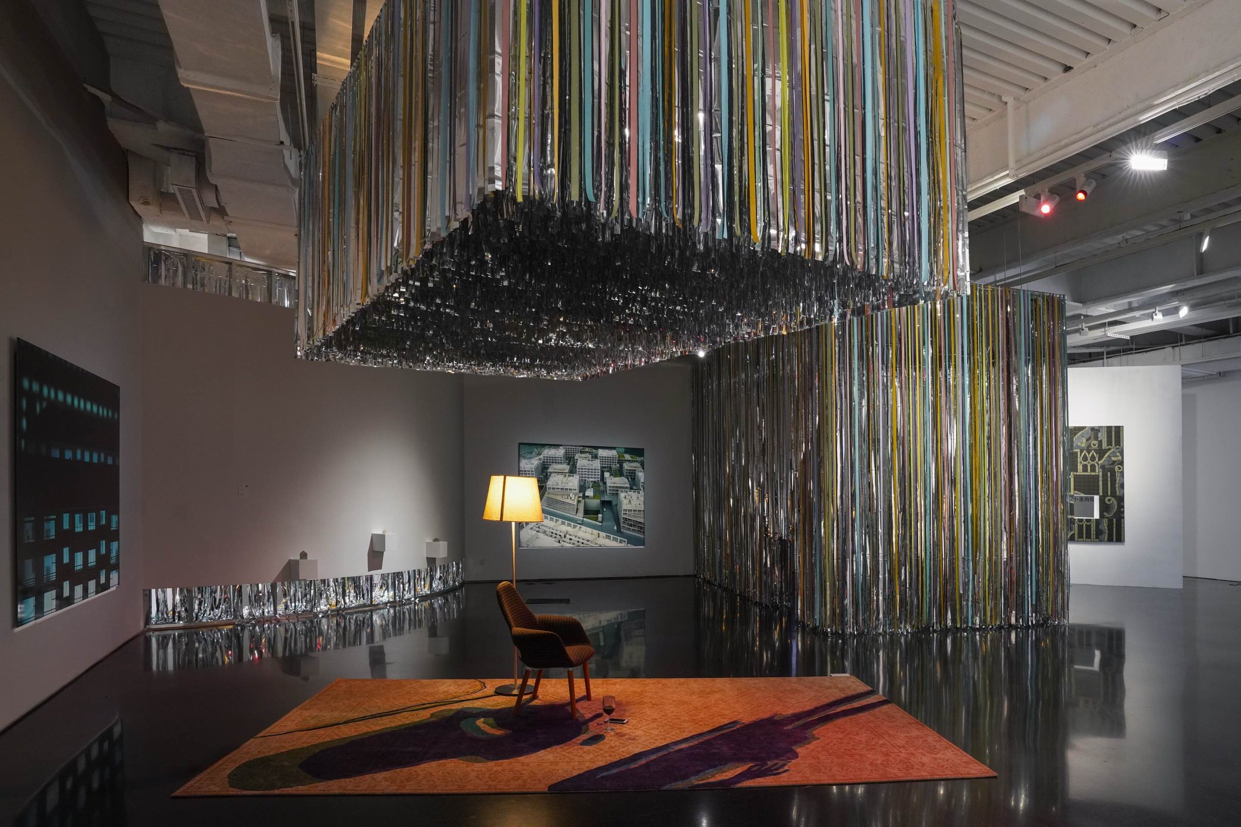 Wide installation view of Danwei Unfolding (2025) at TANK Shanghai, featuring Nishiko's suspended multicoloured ribbon installation above Xing Danwen's orange rug, chair and floor lamp, with Zhi Wei's Puzzle Piece visible on the right-hand wall.