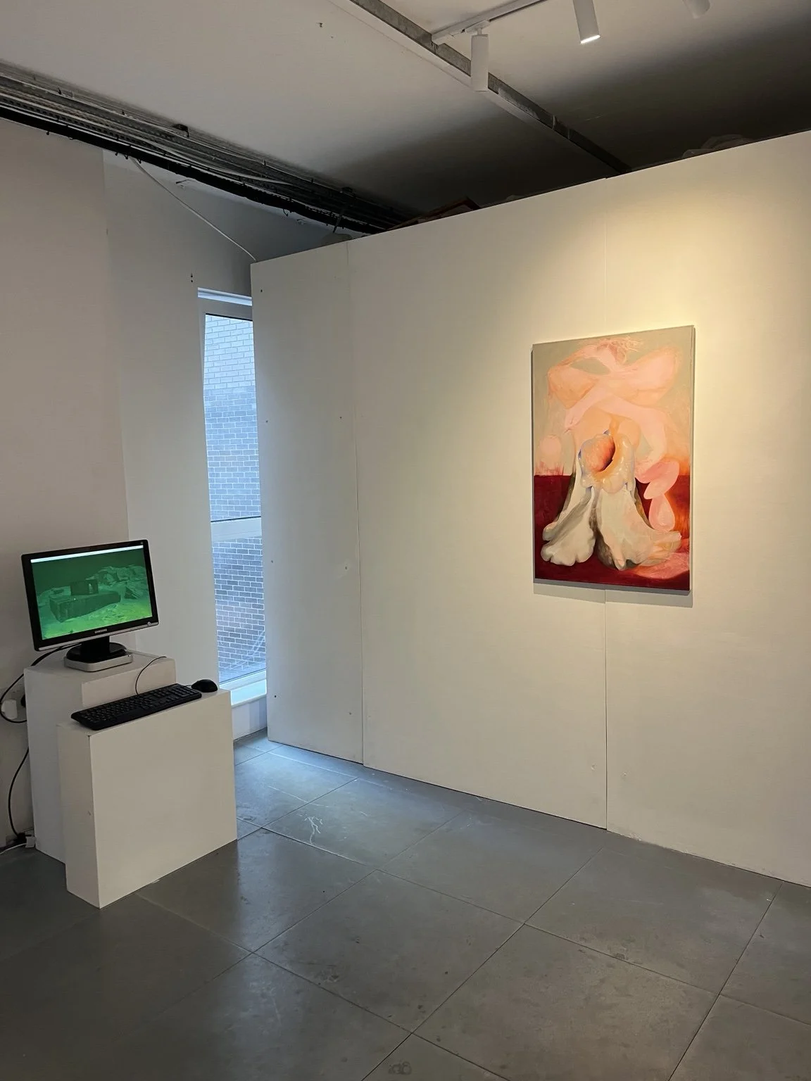 An art gallery exhibit with an abstract painting of a nude figure with soft pink and cream Installation view of Commencement / Commandment (2026) at Prokofiev Studio, London, featuring Harry Payne's interactive digital work Find the Archive (2026) on
