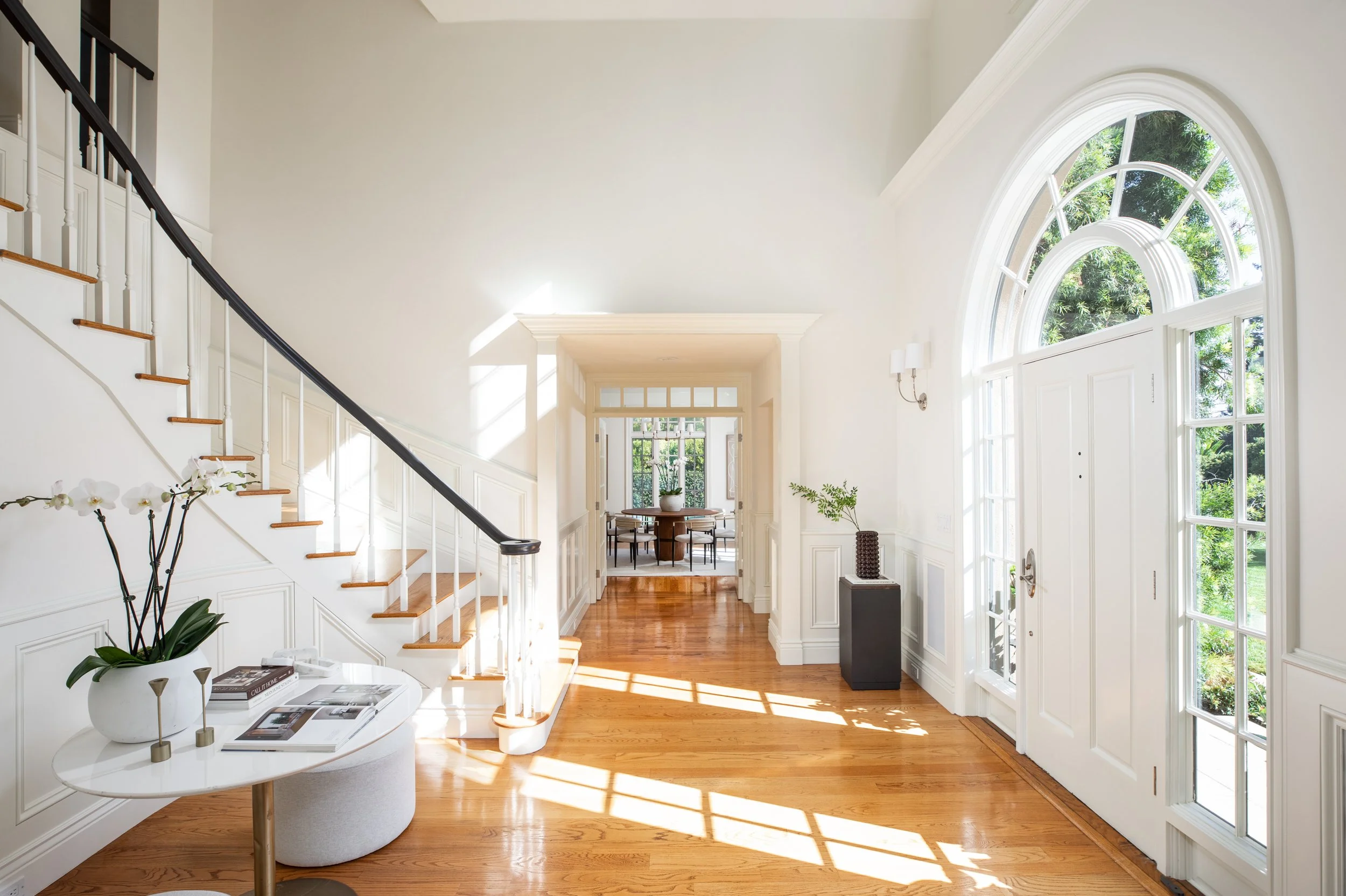 Entryway and staircase with hardwood floors, large arched window, and white walls in a bright, elegant home interior.